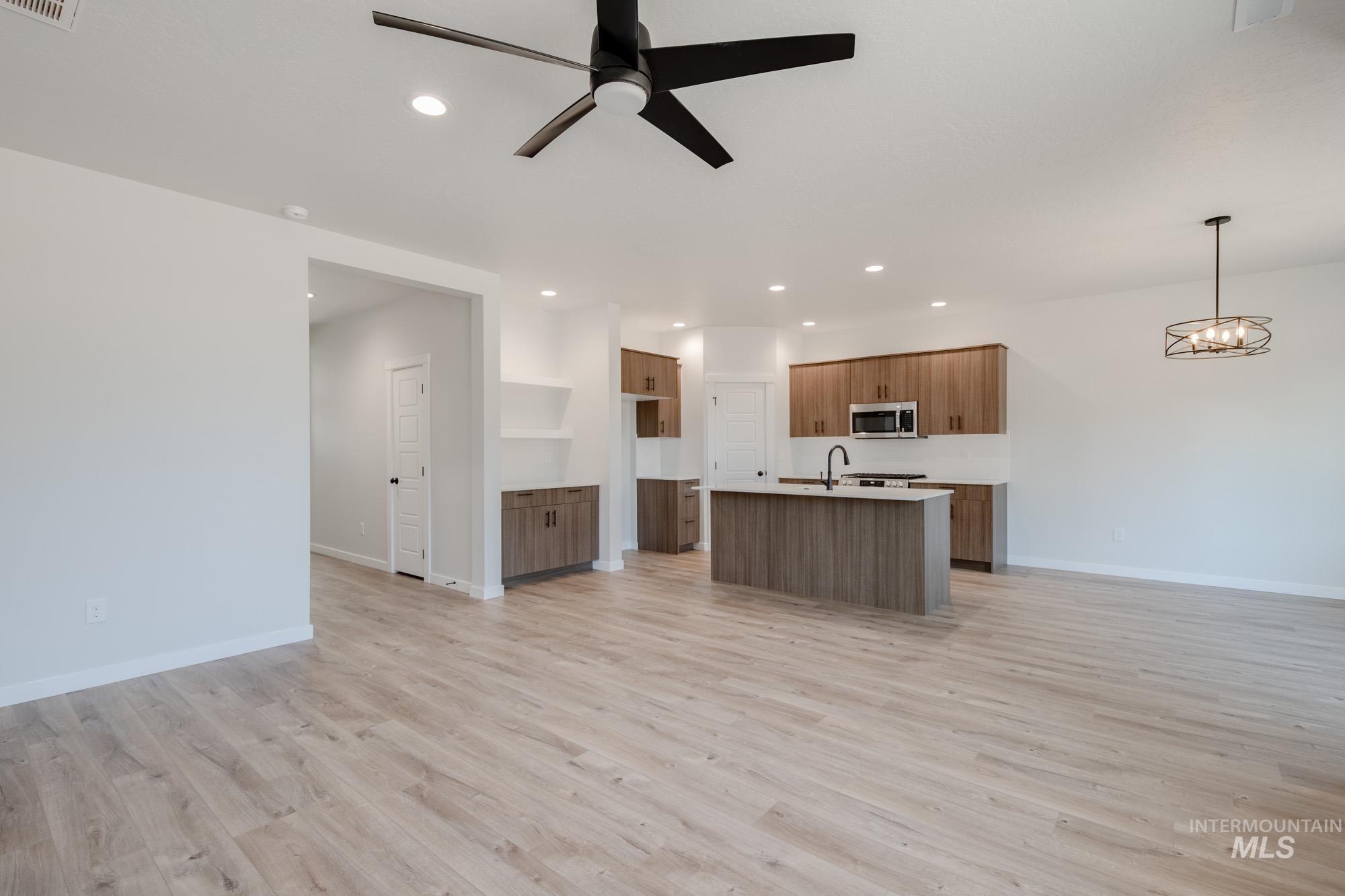 Kitchen featuring open floor plan, a center island with sink, light wood-style floors, a ceiling fan, and decorative light fixtures