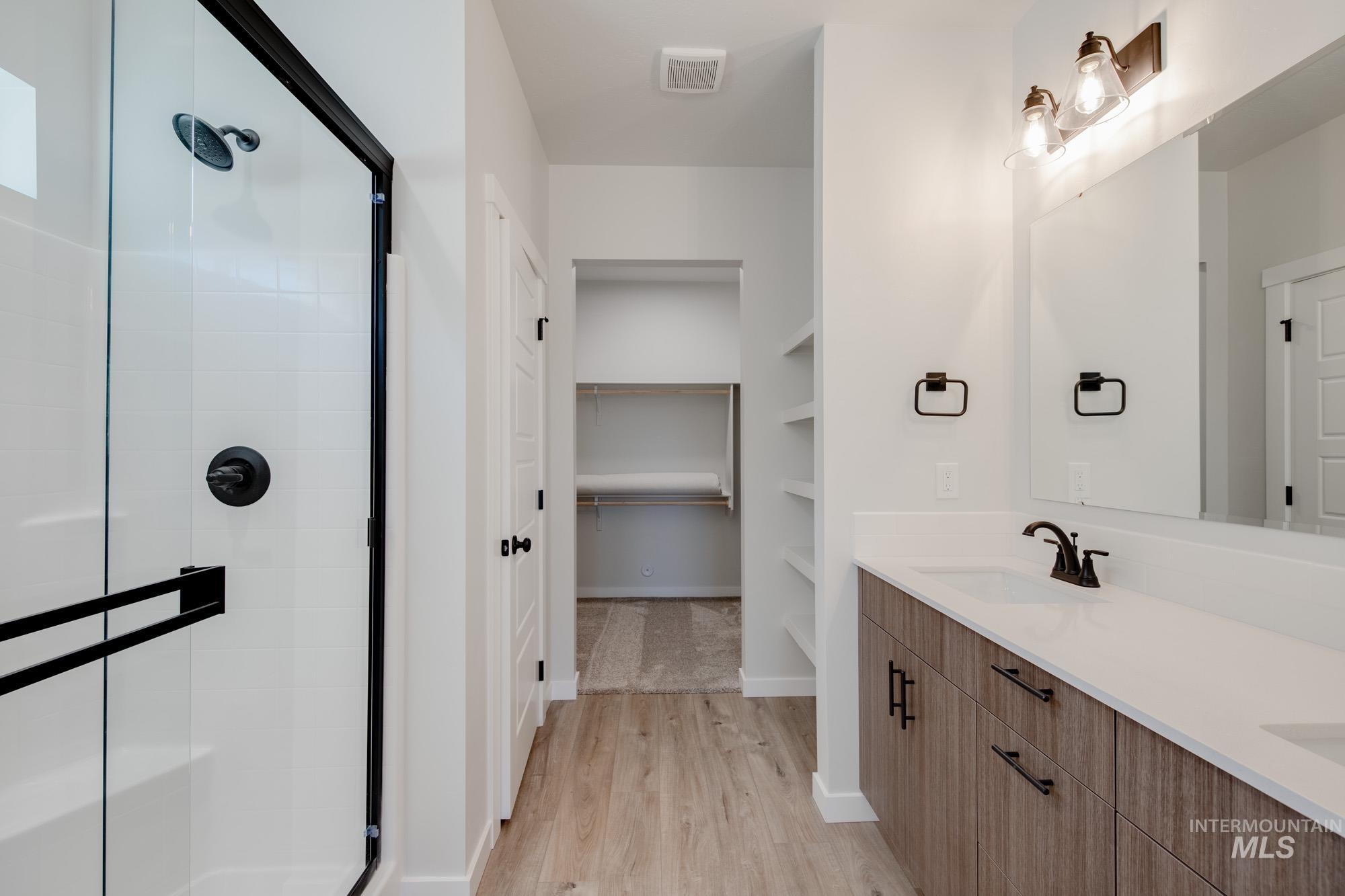 Full bath with a shower stall, double vanity, a spacious closet, light wood finished floors, and built in shelves