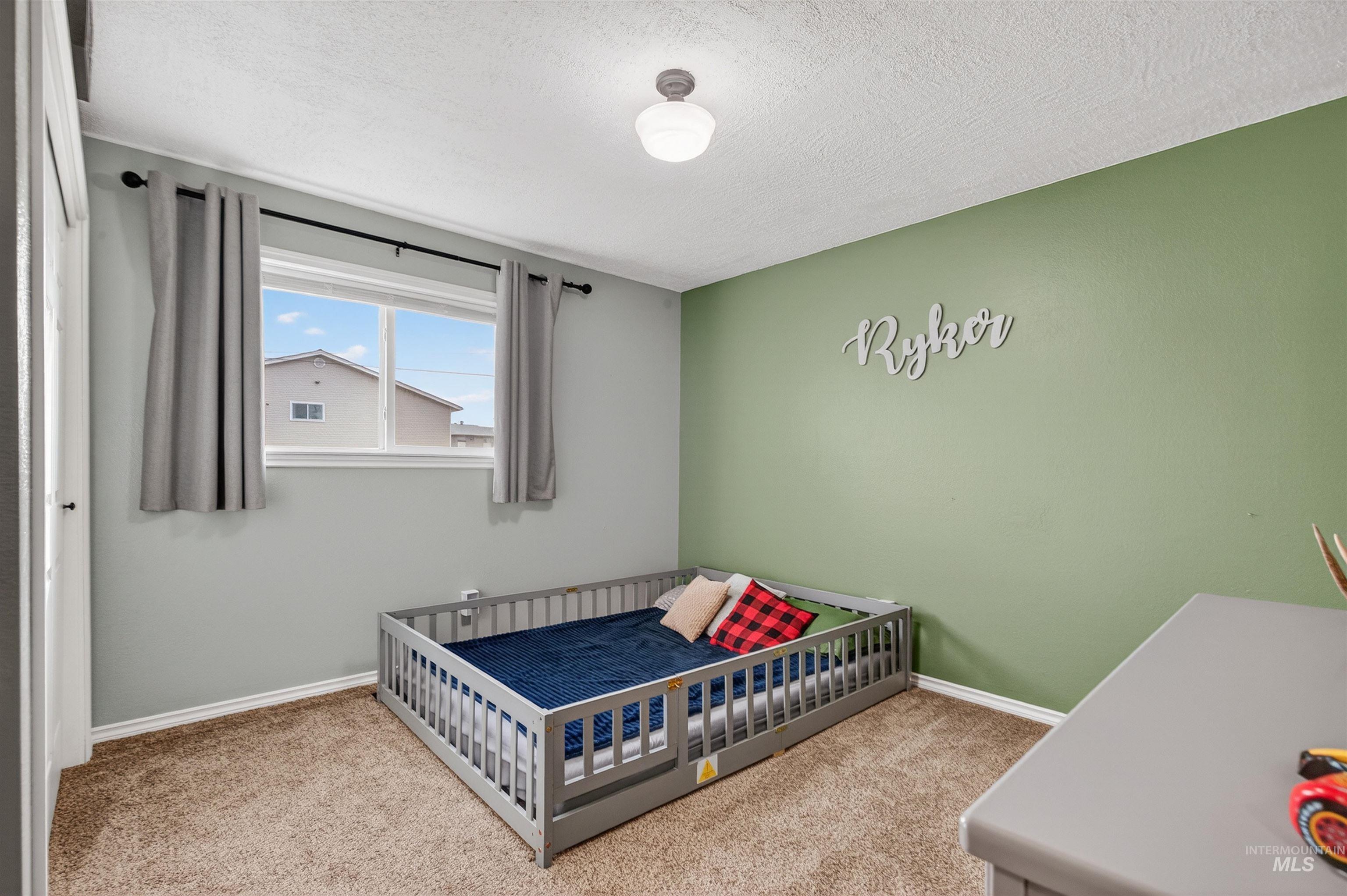 Bedroom with light carpet, a nursery area, and a textured ceiling