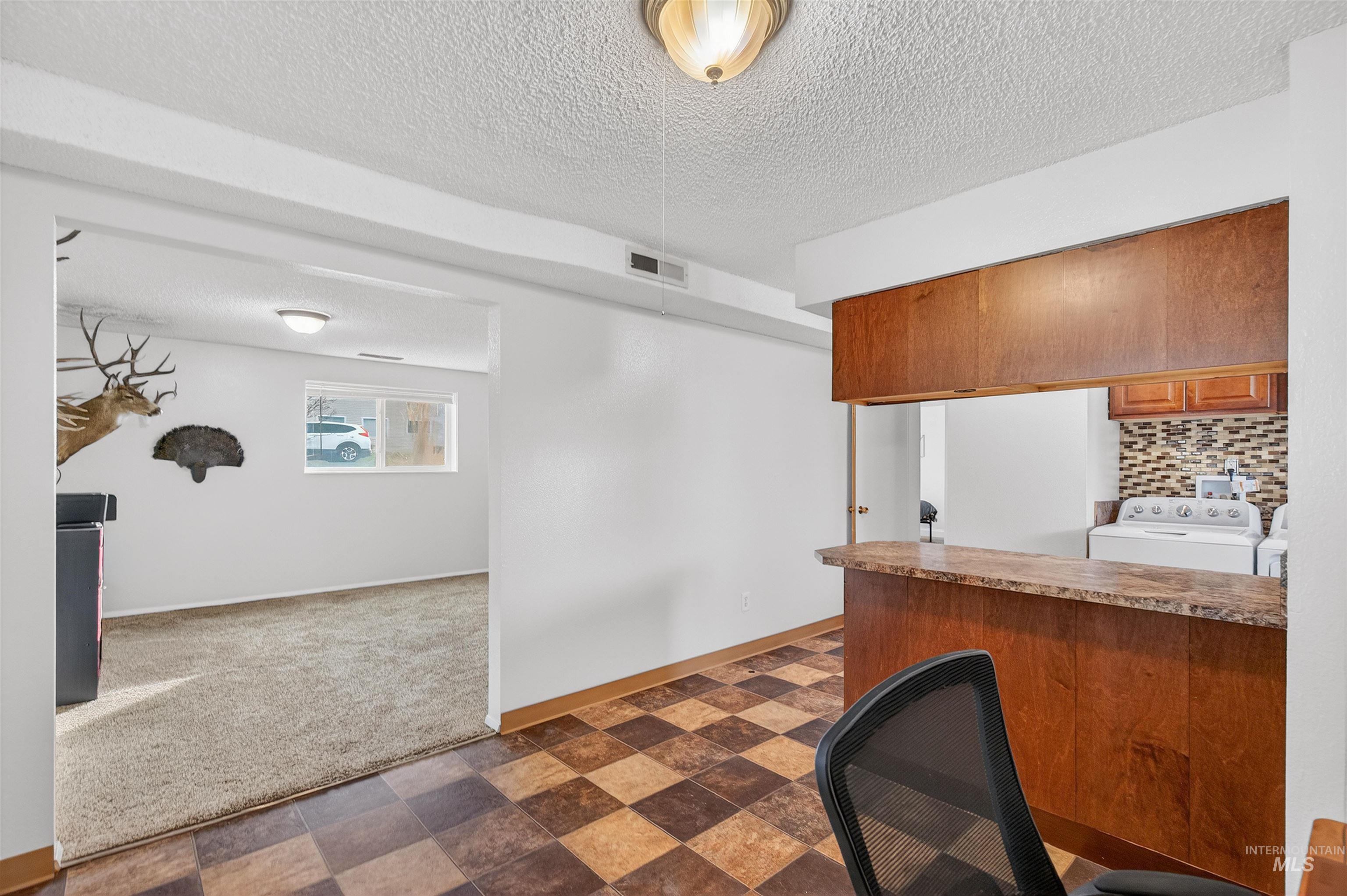 Kitchen featuring wood finish cabinets, a textured ceiling, dark colored carpet, light countertops, and backsplash