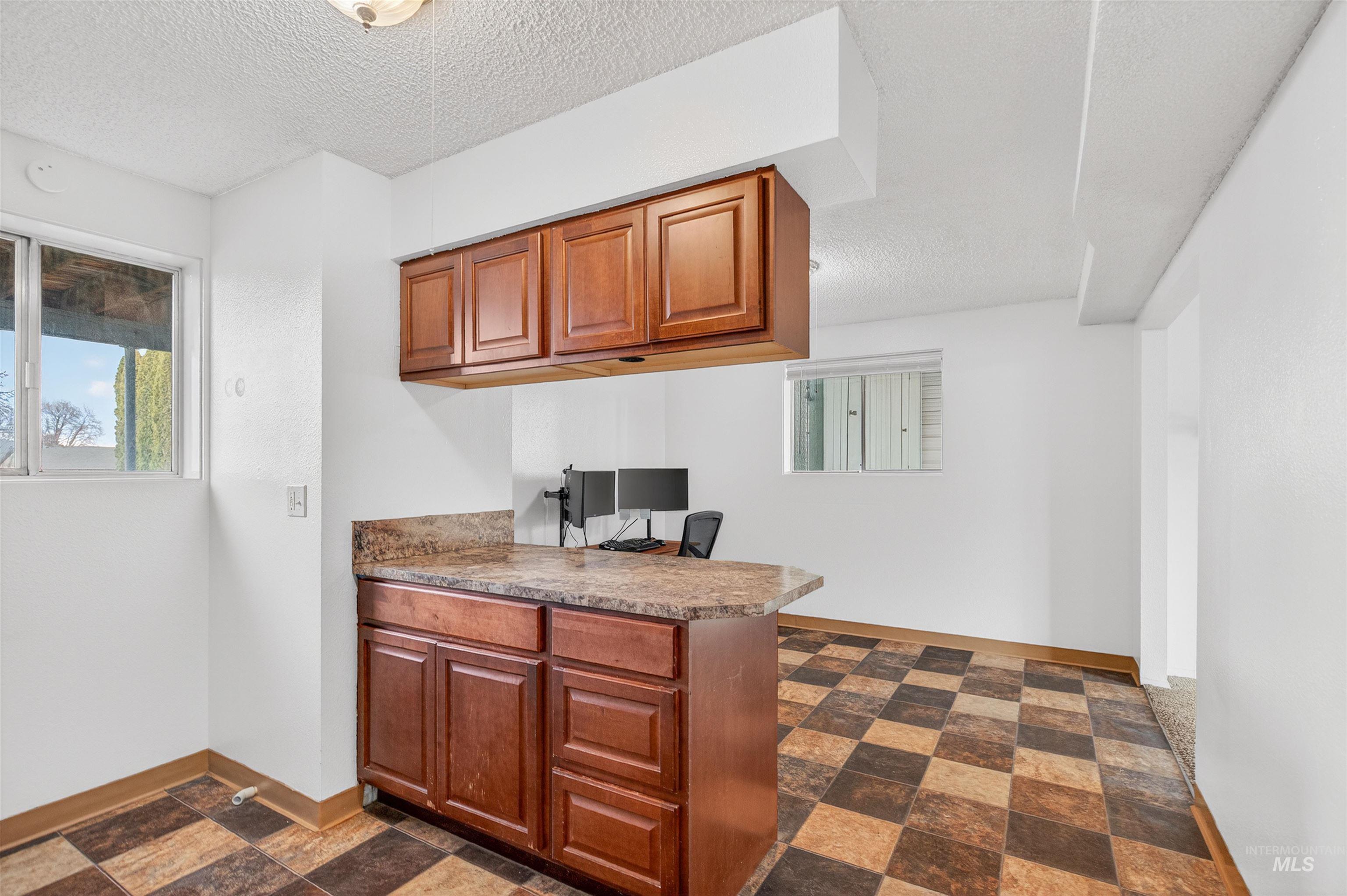 Kitchen featuring a textured ceiling, wood finish cabinets, a peninsula, dark stone finish floors, and an office area
