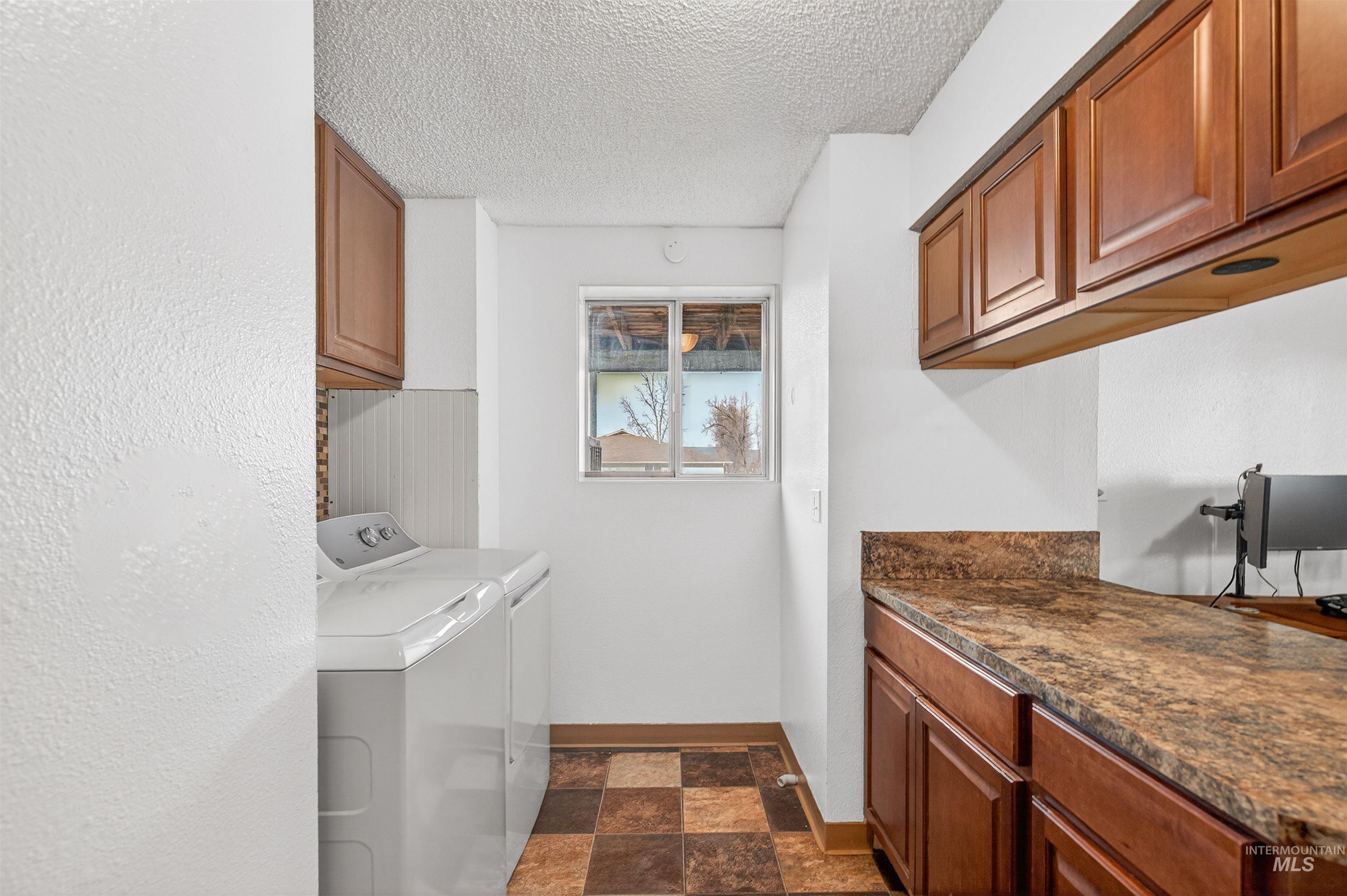 Laundry area featuring cabinet space, a textured ceiling, stone finish flooring, and washer and clothes dryer