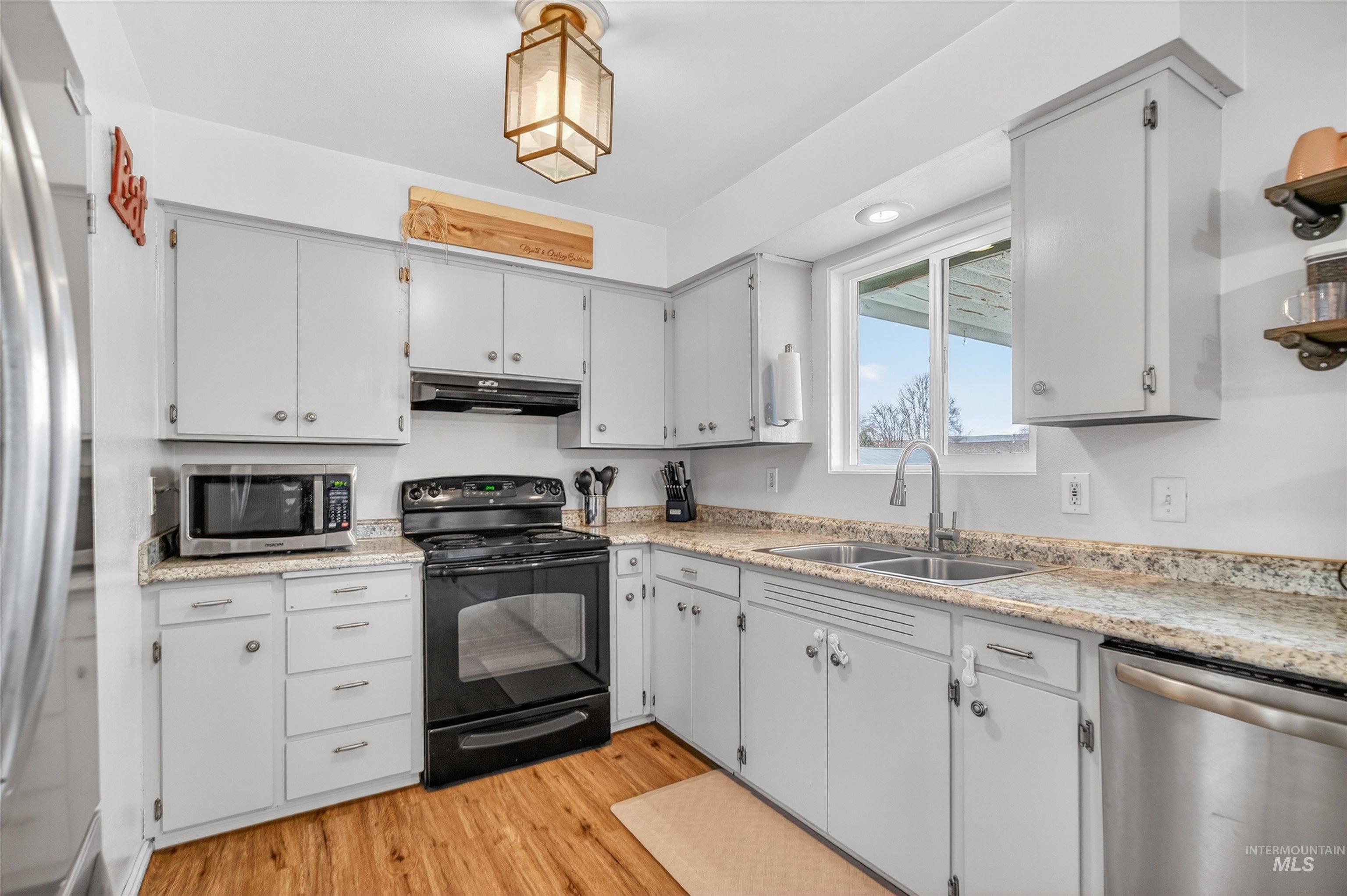 Kitchen featuring stainless steel appliances, light wood-type flooring, white cabinets, and light stone counters