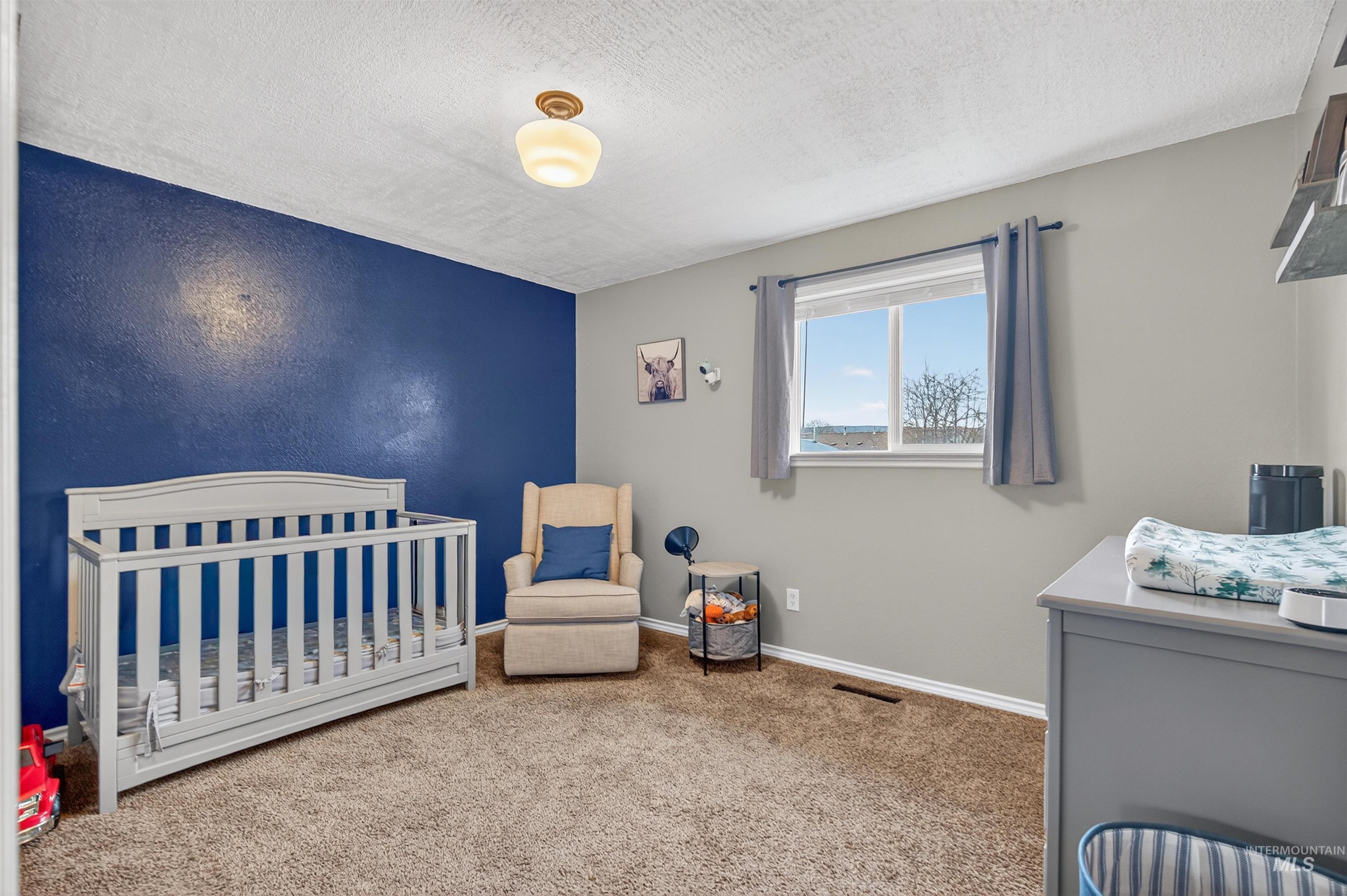 Bedroom with carpet, a nursery area, and a textured ceiling