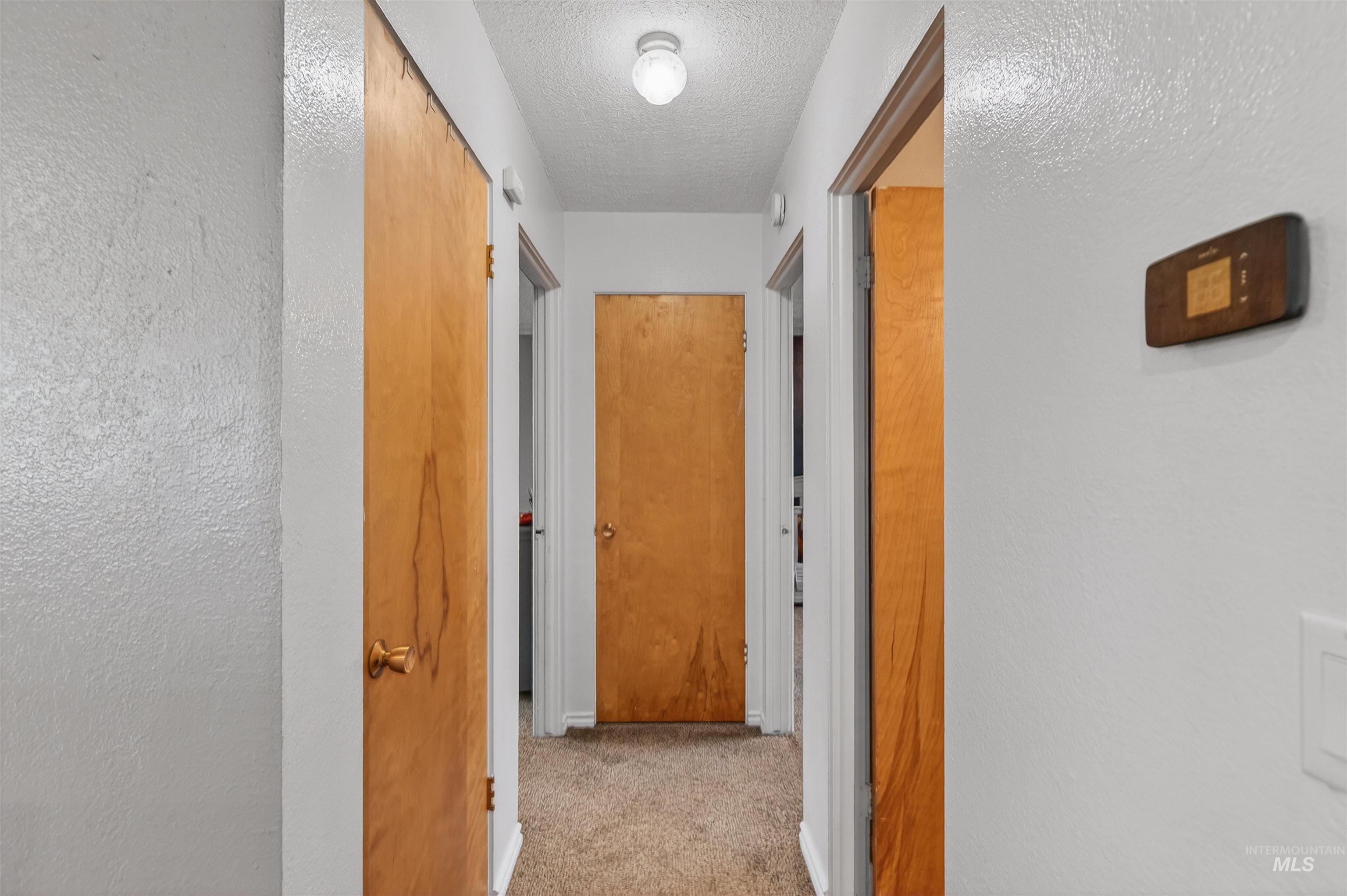 Hall featuring a textured wall, light carpet, and a textured ceiling