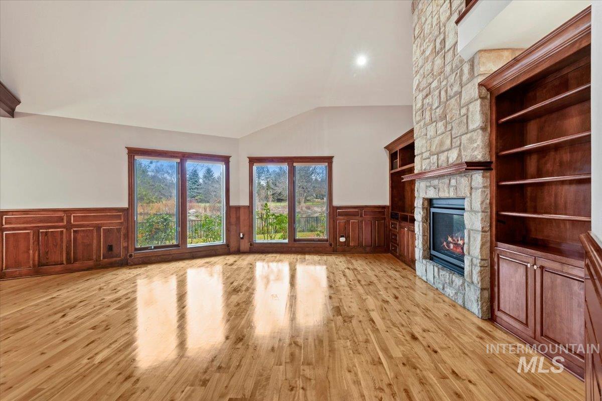 Unfurnished living room with a fireplace, lofted ceiling, light wood-style flooring, wainscoting, and built in features
