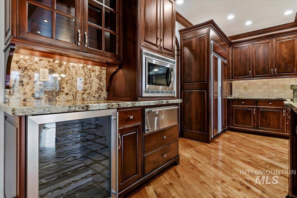 Kitchen with beverage cooler, a warming drawer, light stone countertops, glass insert cabinets, and decorative backsplash