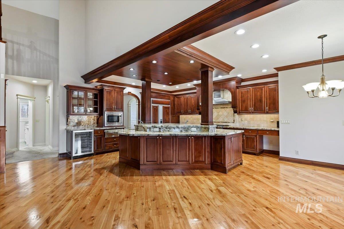 Kitchen with backsplash, glass insert cabinets, beverage cooler, a chandelier, and light stone counters
