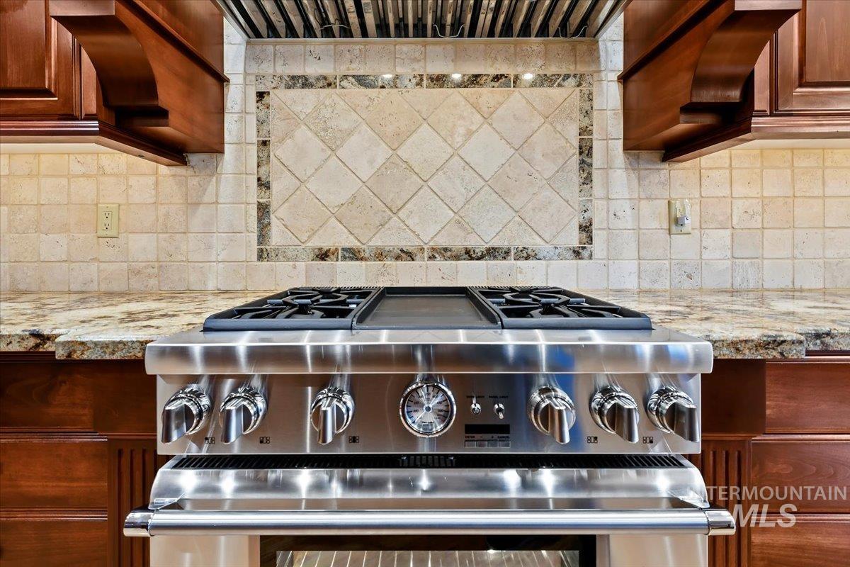 Kitchen with stainless steel range with gas stovetop, light stone counters, backsplash, and custom exhaust hood