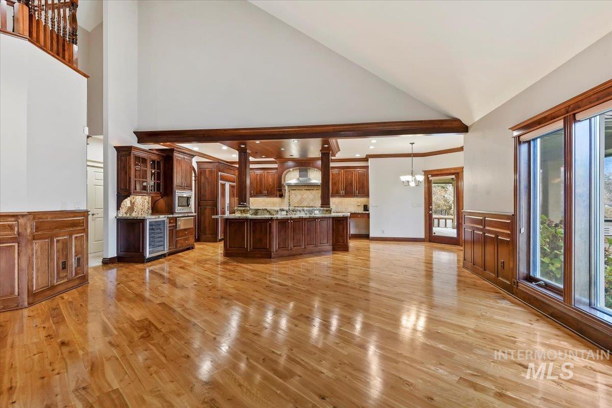 Kitchen with a chandelier, light wood-type flooring, an island with sink, glass insert cabinets, and wine cooler