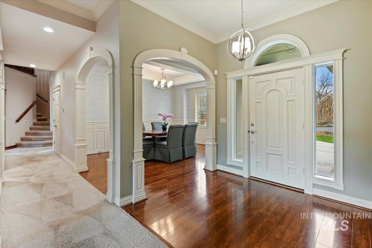 Entryway with ornamental molding, dark wood-style flooring, a chandelier, arched walkways, and stairs