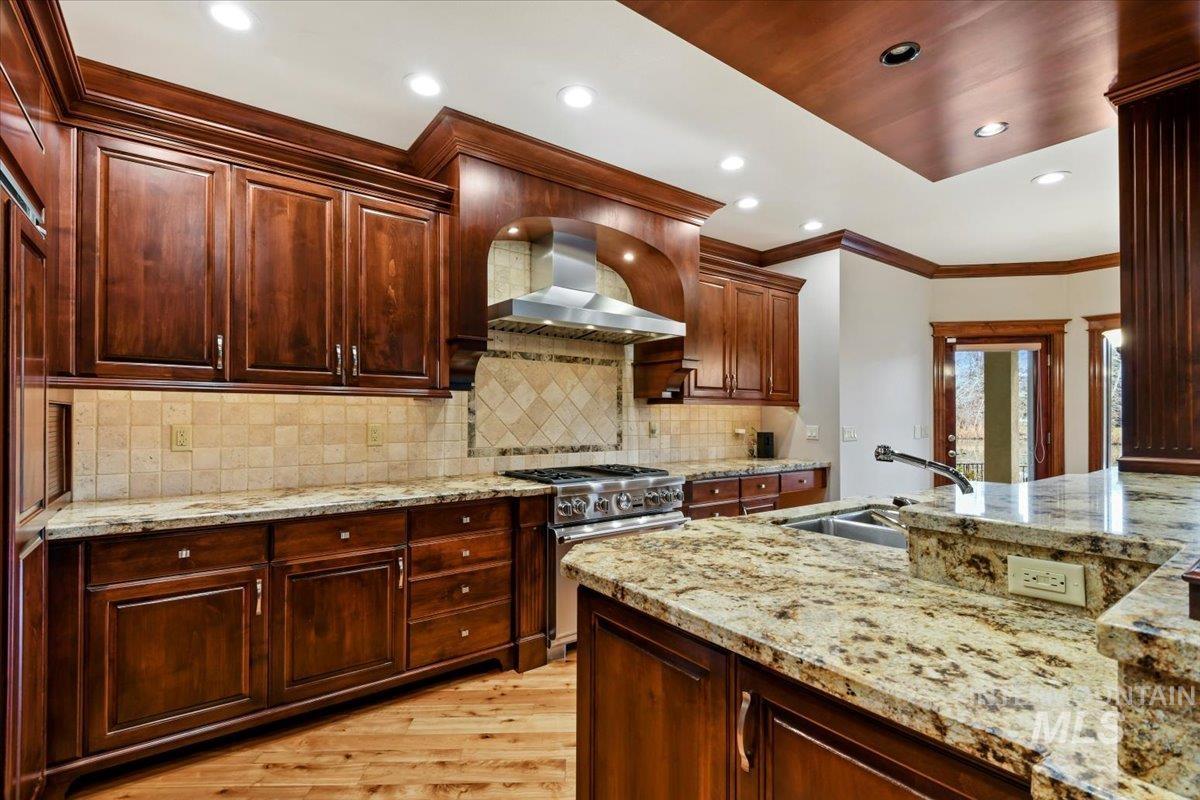 Kitchen featuring light stone counters, wall chimney exhaust hood, high end stainless steel range oven, crown molding, and recessed lighting