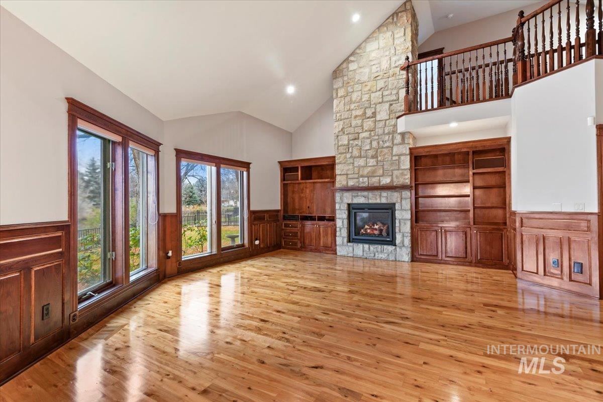 Unfurnished living room with wainscoting, high vaulted ceiling, a fireplace, light wood-style floors, and recessed lighting