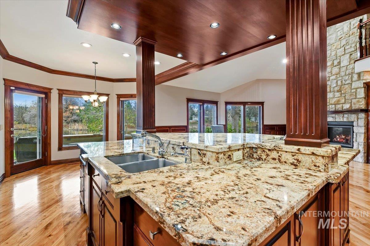 Kitchen featuring brown cabinets, lofted ceiling, light stone countertops, light wood-style flooring, and pendant lighting
