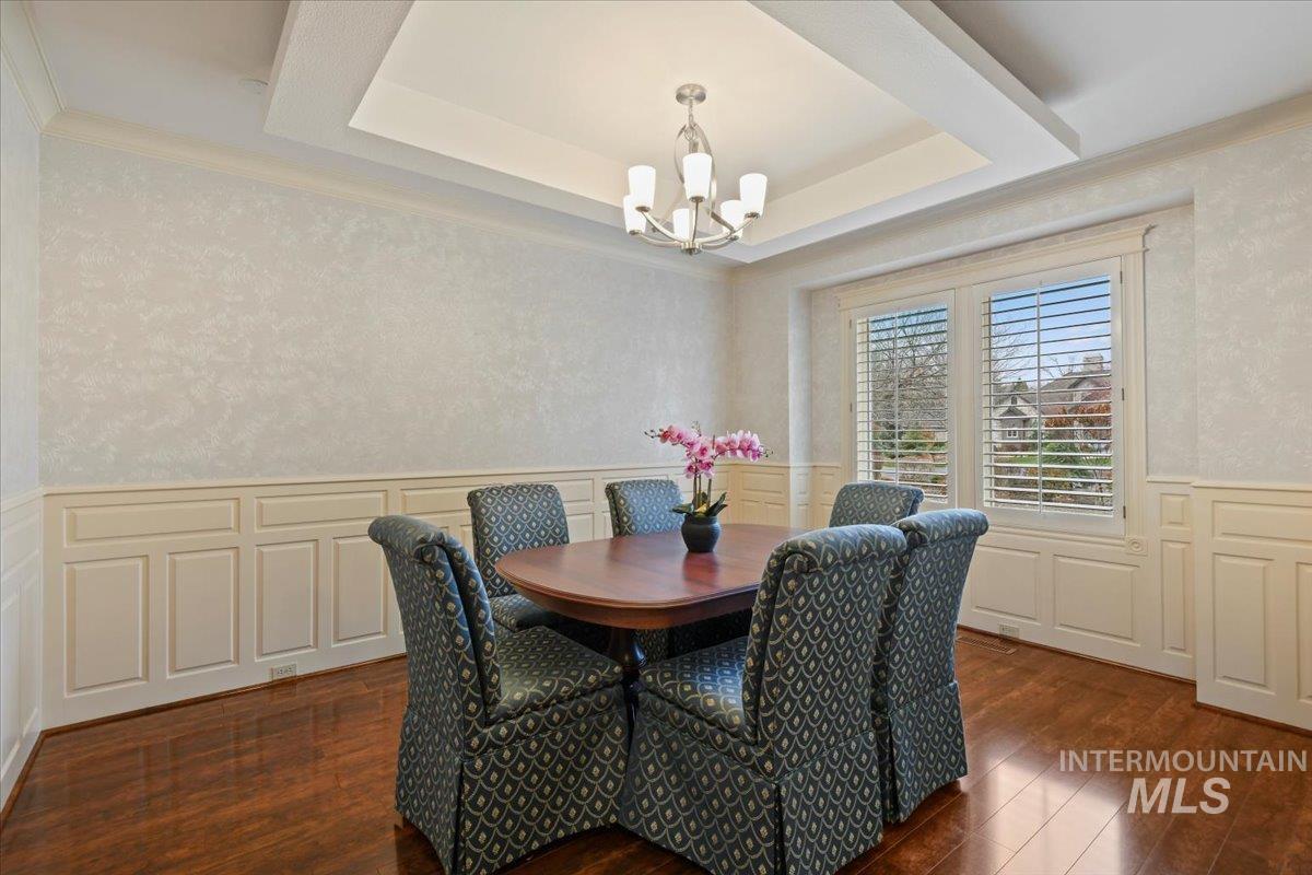 Dining space featuring a wainscoted wall, a decorative wall, dark wood-style floors, ornamental molding, and a tray ceiling