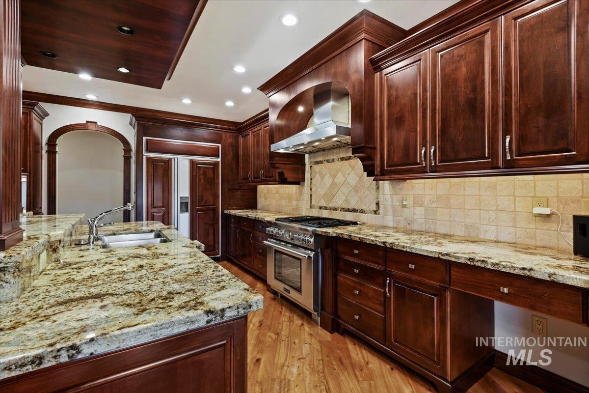 Kitchen with light stone countertops, premium appliances, wall chimney exhaust hood, dark brown cabinetry, and recessed lighting