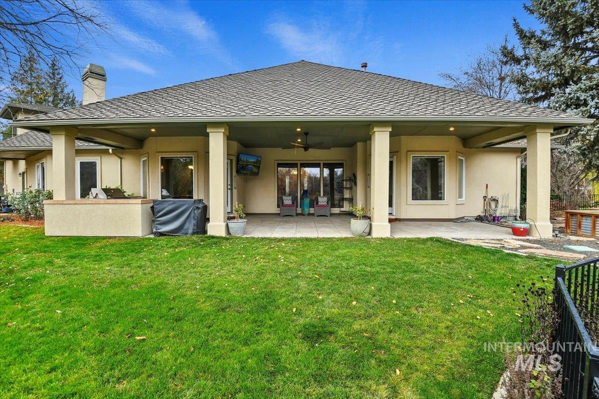 Rear view of property featuring stucco siding, a ceiling fan, a patio, and a lawn