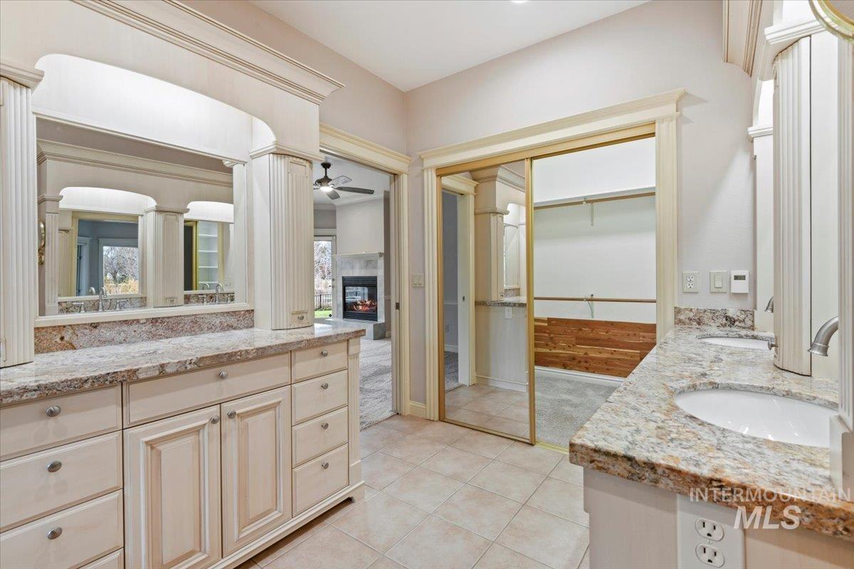 Bathroom with double vanity, a walk in closet, a glass covered fireplace, light tile patterned floors, and ornate columns