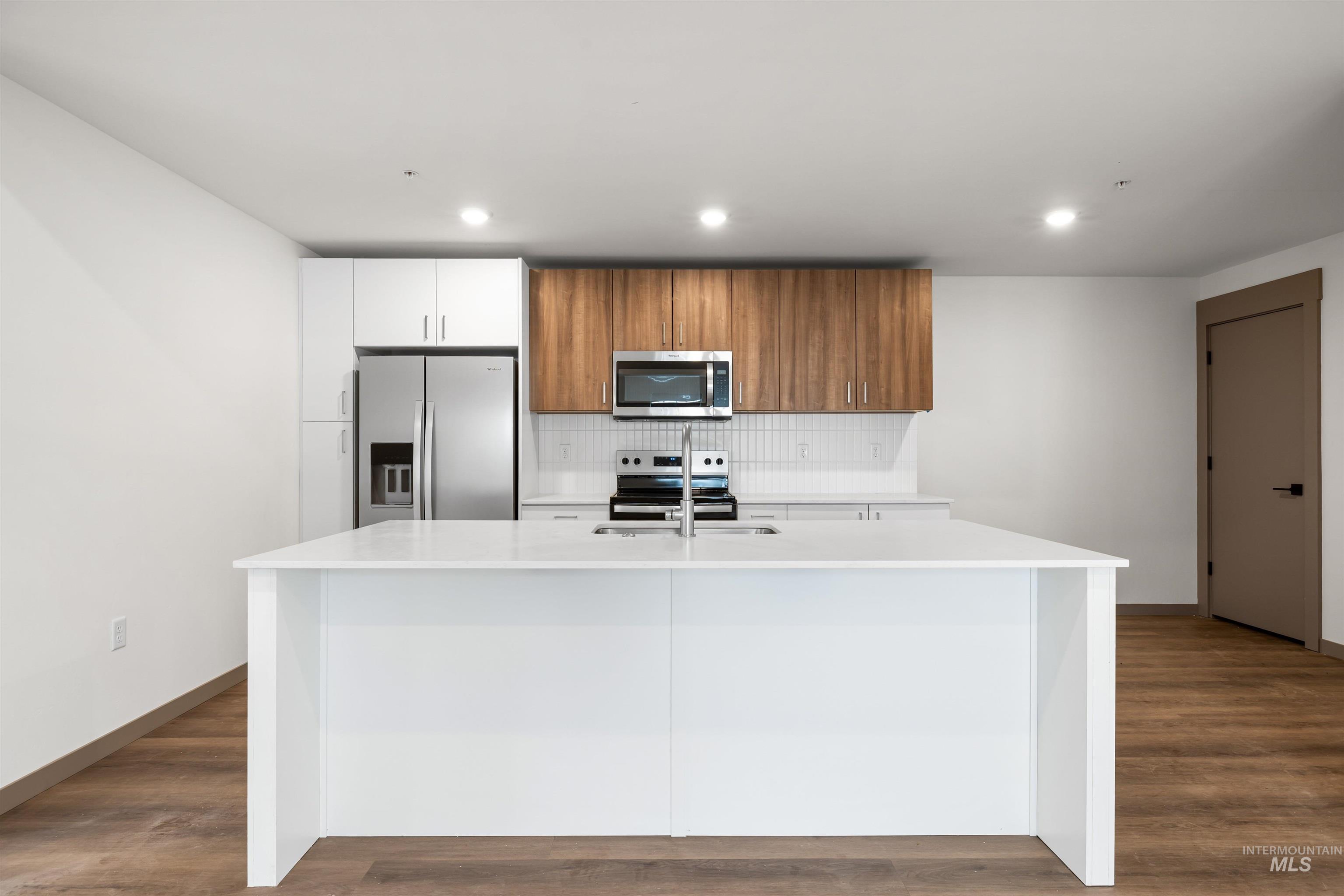 Kitchen featuring brown cabinets, tasteful backsplash, stainless steel appliances, a kitchen island with sink, and white cabinets