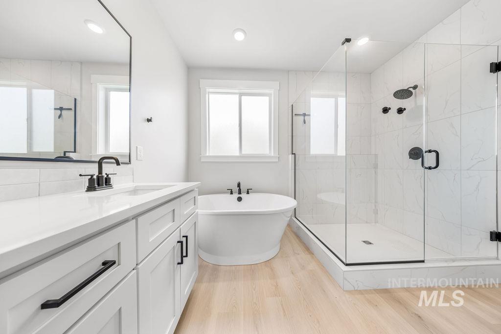 Bathroom featuring a marble finish shower, a freestanding tub, vanity, light wood finished floors, and recessed lighting