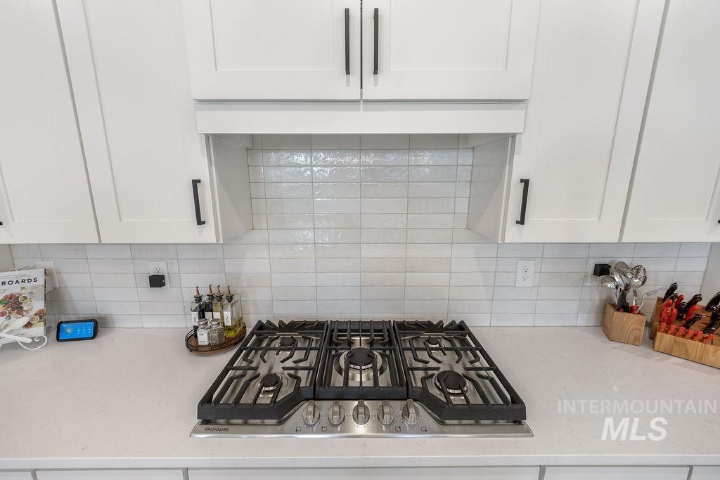 Kitchen view of stainless steel gas stovetop, tasteful backsplash, and white cabinets