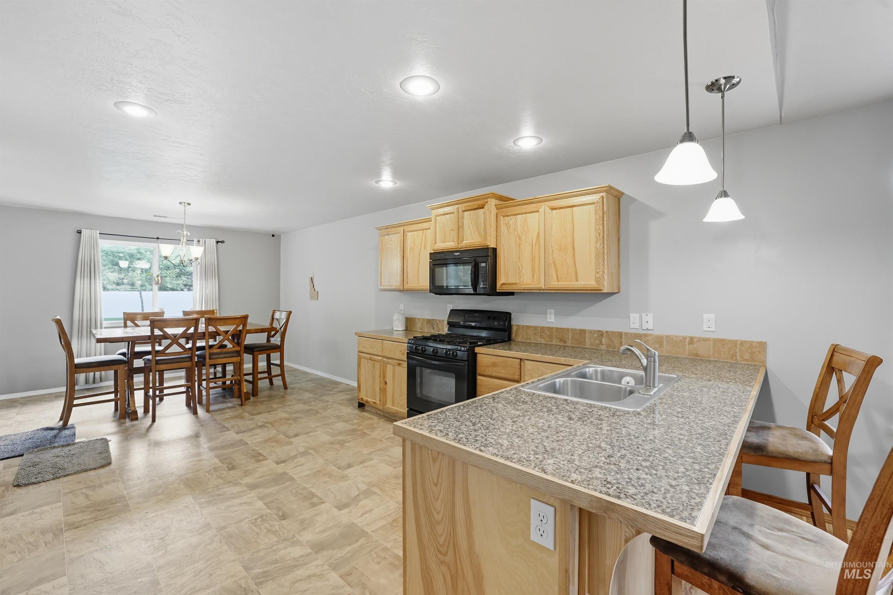 Kitchen featuring pendant lighting, a kitchen breakfast bar, light brown cabinets, black appliances, and a peninsula