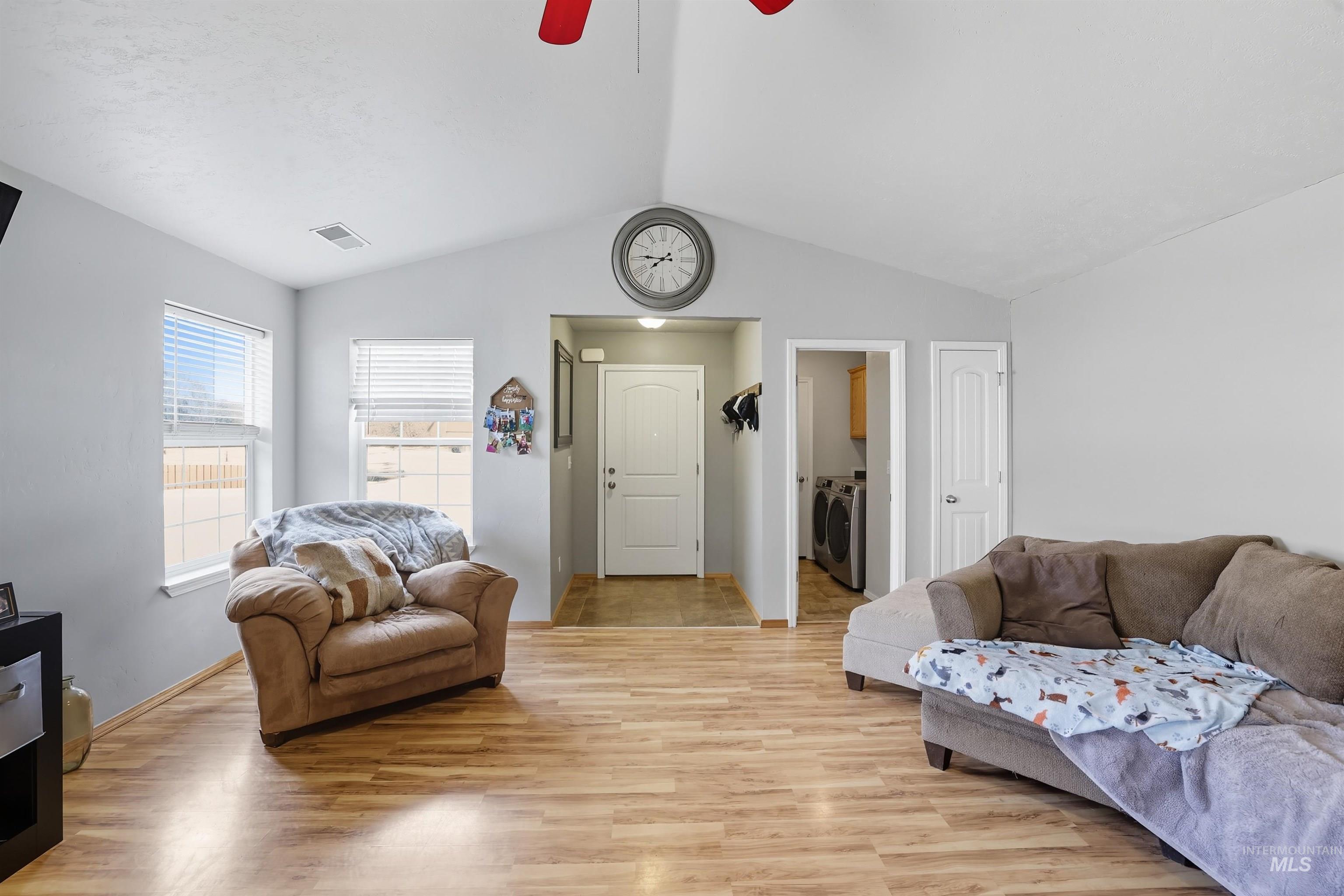 Living room featuring vaulted ceiling, light wood-style floors, separate washer and dryer, and ceiling fan