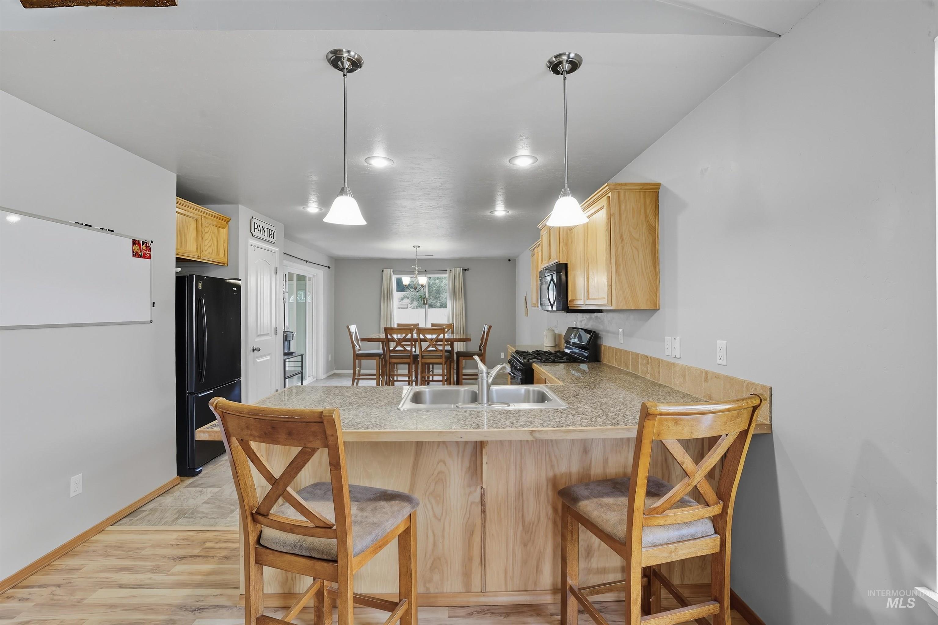 Kitchen with a breakfast bar, light brown cabinets, hanging light fixtures, black appliances, and a peninsula