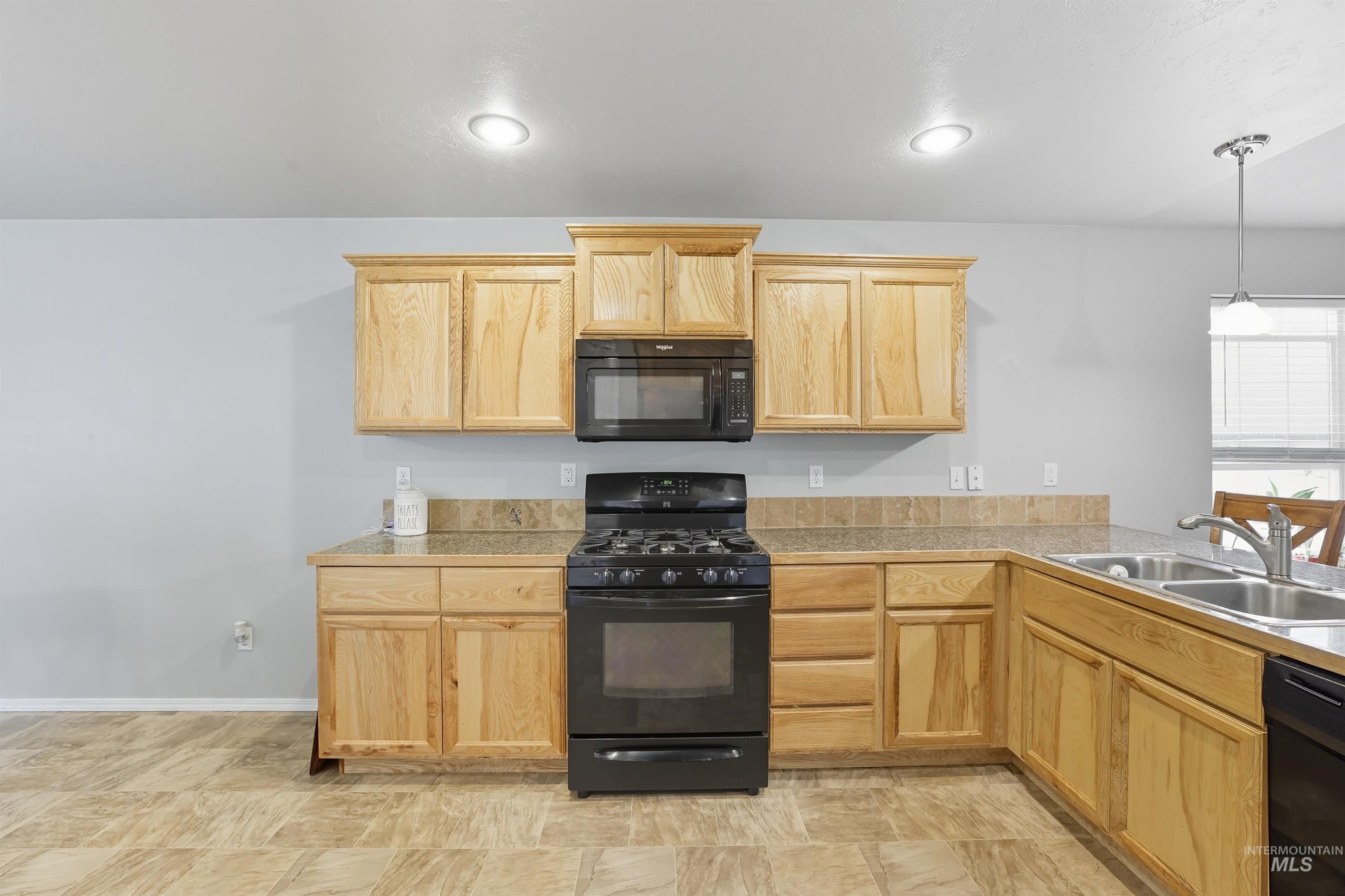 Kitchen featuring black appliances, light brown cabinets, tile counters, and hanging light fixtures