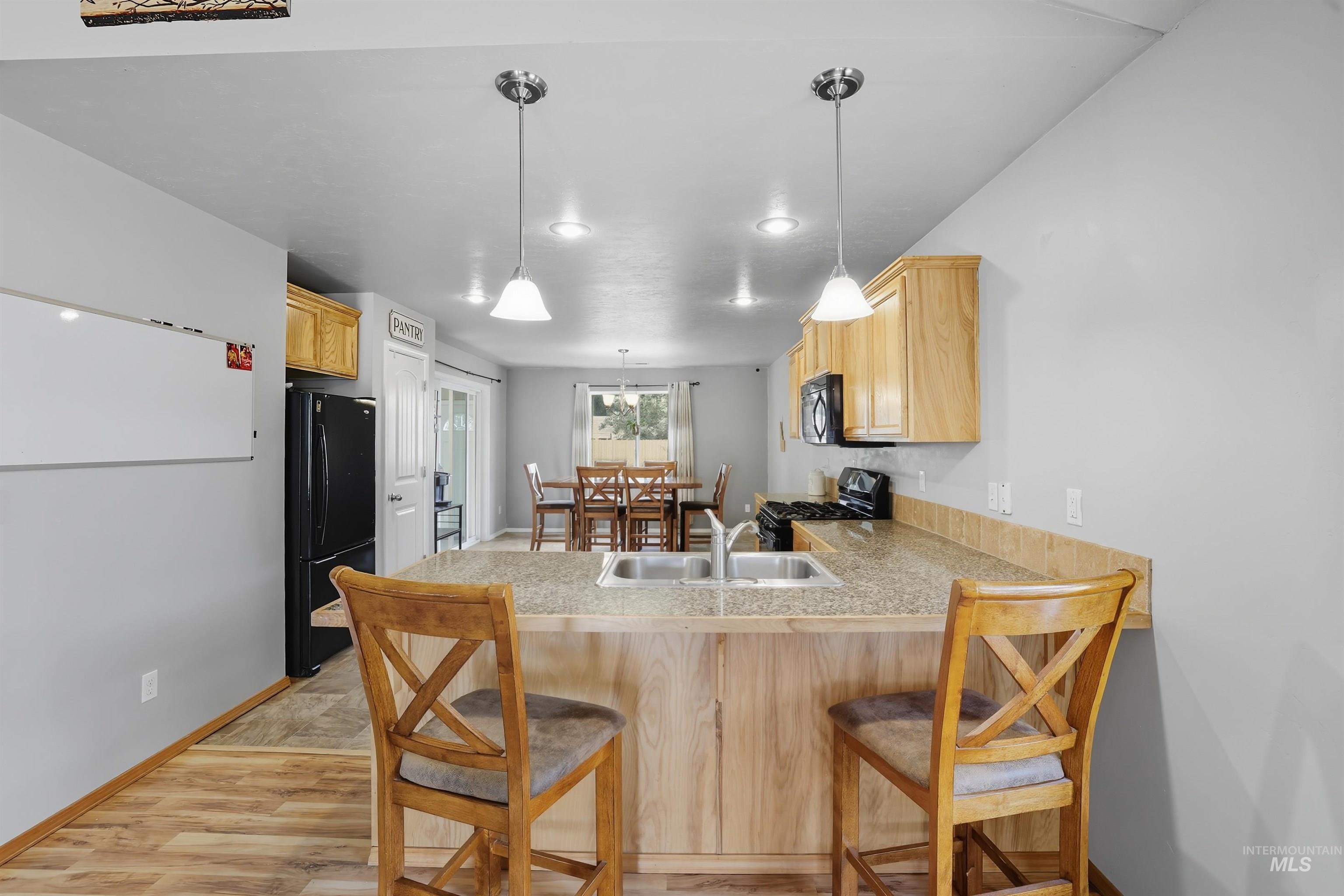 Kitchen with a breakfast bar area, light brown cabinetry, light wood finished floors, black appliances, and a peninsula