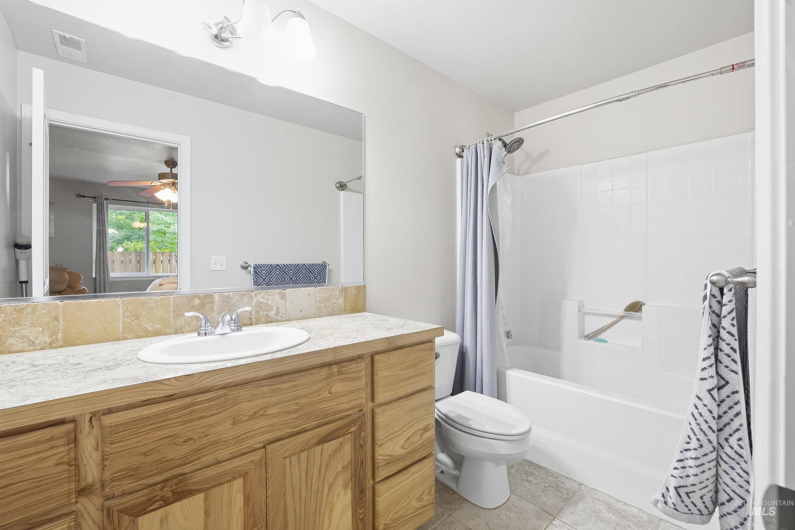Full bathroom with shower / tub combo with curtain, vanity, light tile patterned floors, and ceiling fan