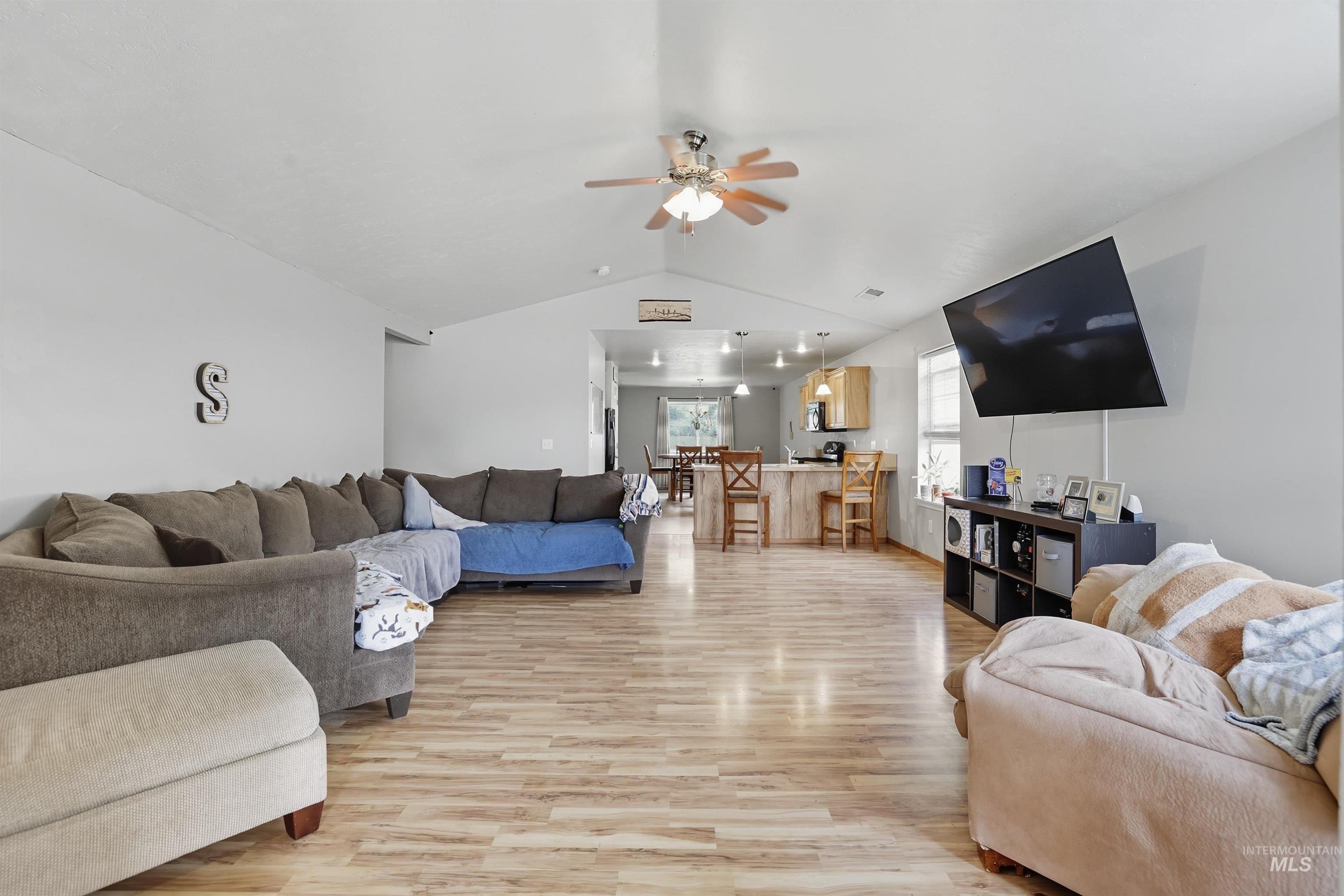 Living room featuring vaulted ceiling, light wood finished floors, and ceiling fan
