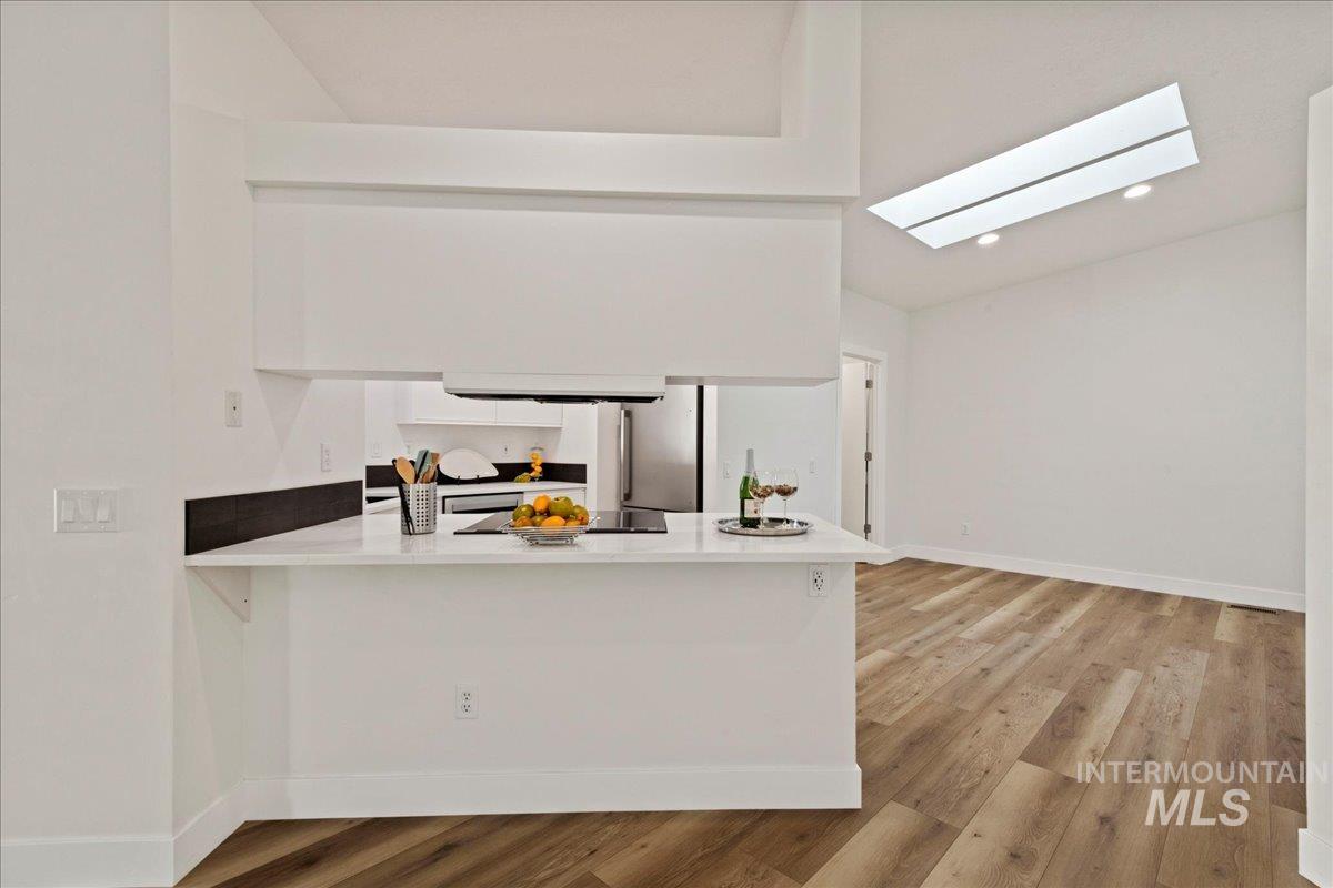 Kitchen with light wood finished floors, light stone countertops, a skylight, a peninsula, and recessed lighting