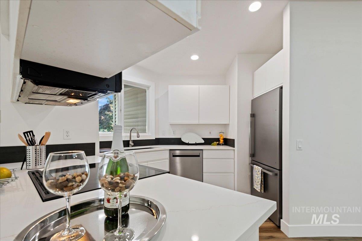 Kitchen with white cabinetry, wood finished floors, recessed lighting, stainless steel appliances, and range hood