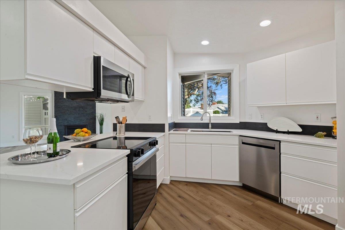 Kitchen with appliances with stainless steel finishes, white cabinetry, recessed lighting, light wood-style flooring, and a peninsula
