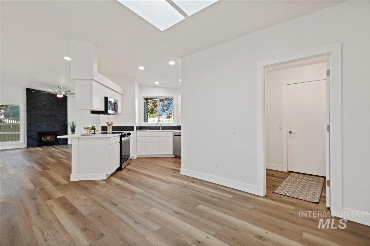 Kitchen featuring open floor plan, white cabinets, light countertops, a large fireplace, and a skylight