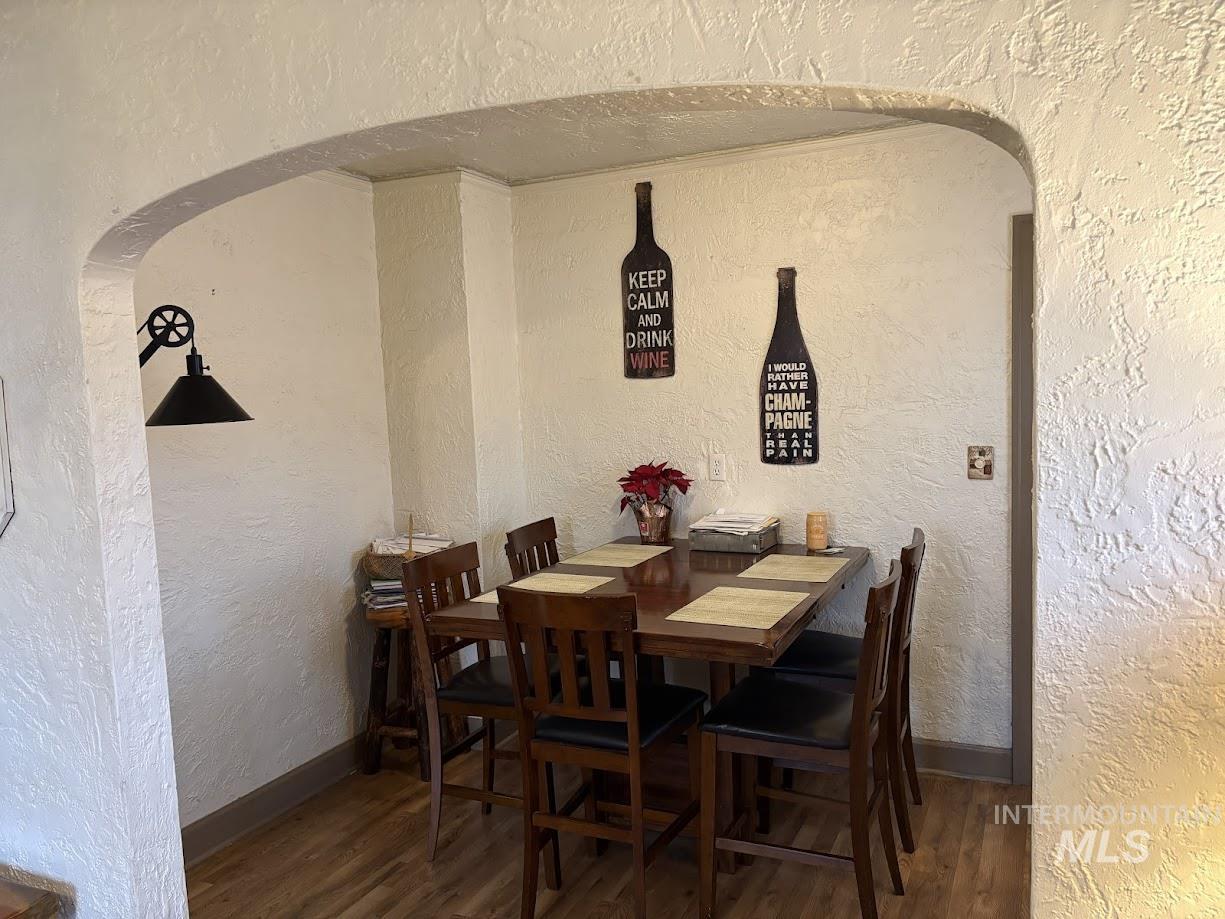 Dining area with a textured wall, arched walkways, and dark wood-type flooring
