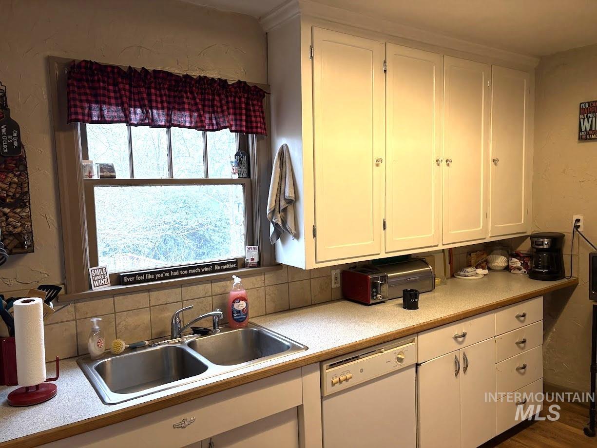 Kitchen with light countertops, white cabinetry, white dishwasher, a textured wall, and tasteful backsplash