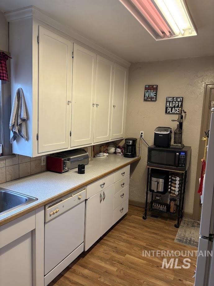 Kitchen with white cabinetry, light countertops, dark wood-style flooring, white appliances, and a textured wall