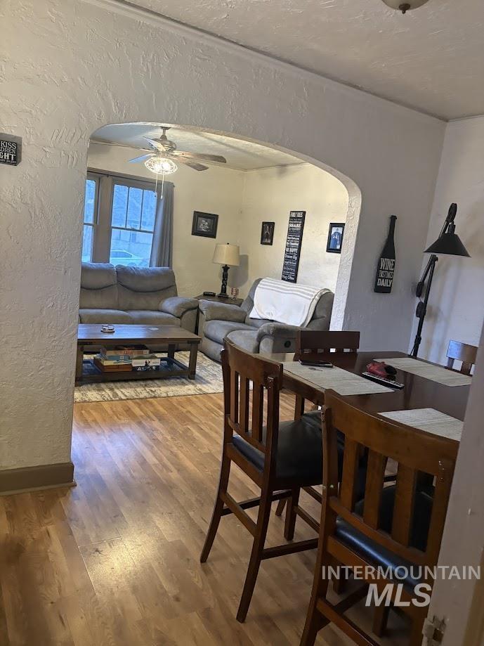 Dining area with a textured wall, arched walkways, wood finished floors, and ceiling fan