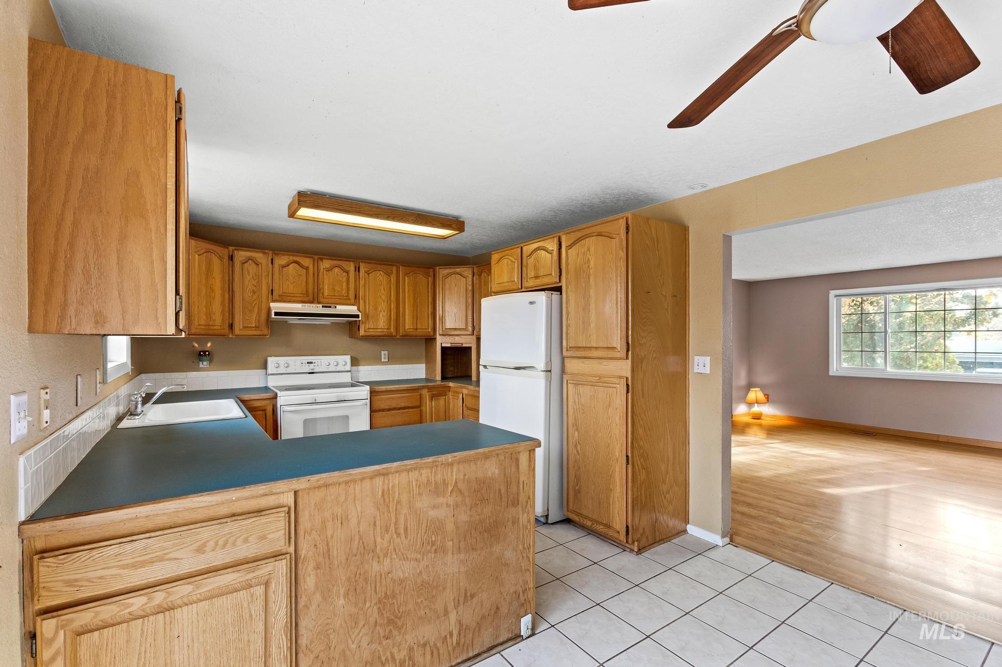 Kitchen featuring a peninsula, light tile patterned floors, white appliances, under cabinet range hood, and brown cabinetry