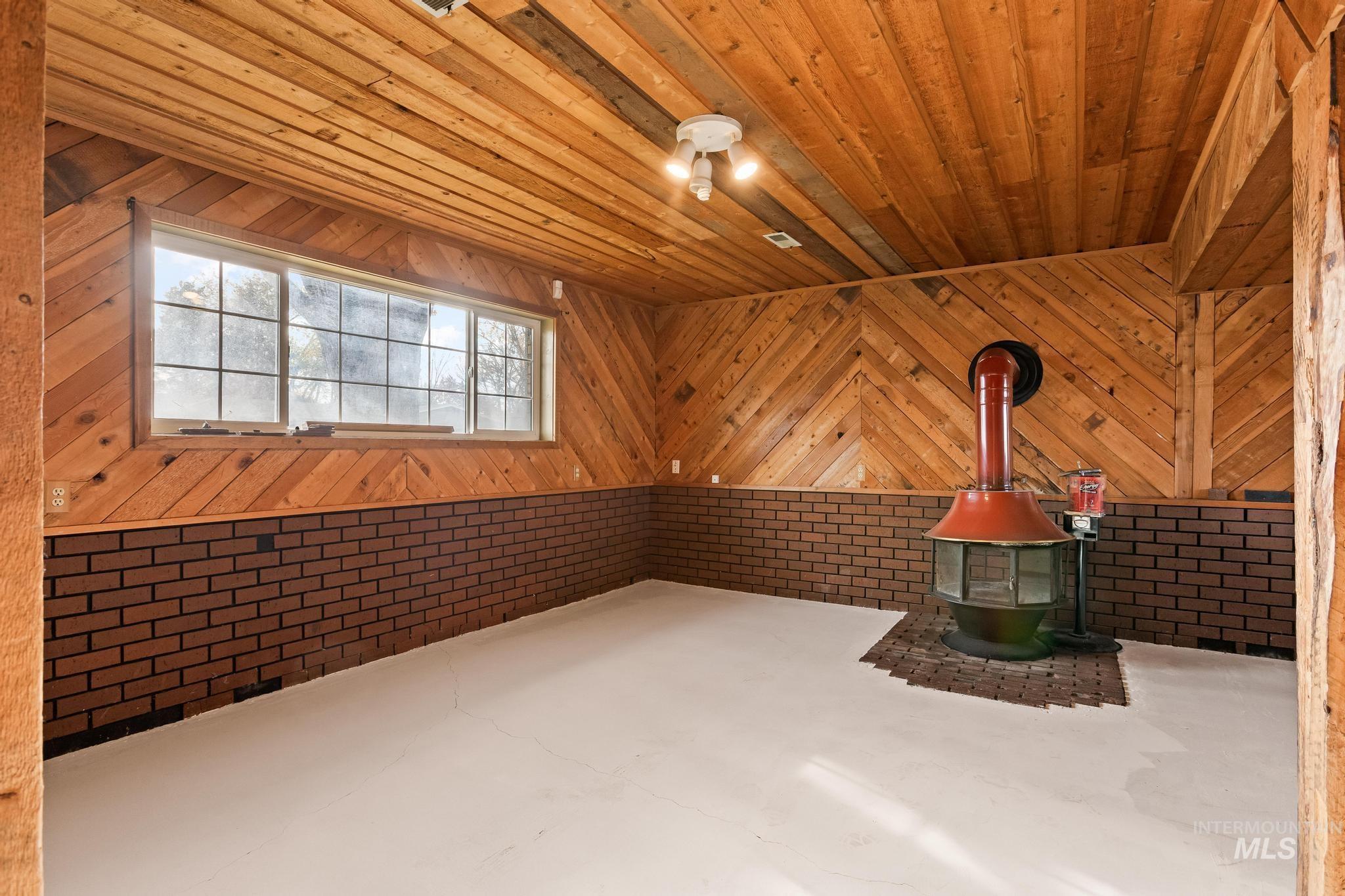 Unfurnished room featuring a wood stove, wooden ceiling, and finished concrete flooring
