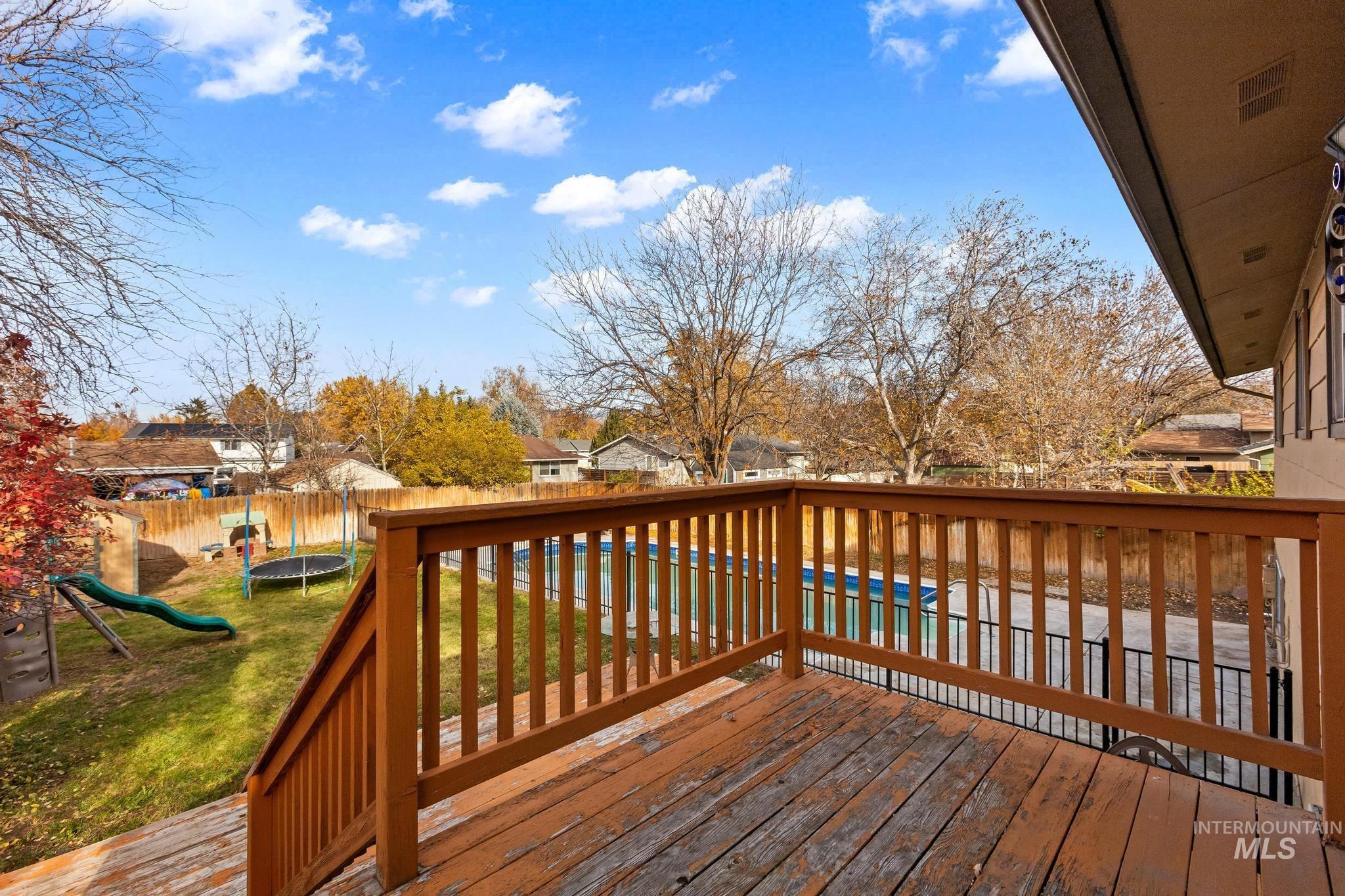 Wooden deck with a trampoline, a fenced backyard, a residential view, and a playground