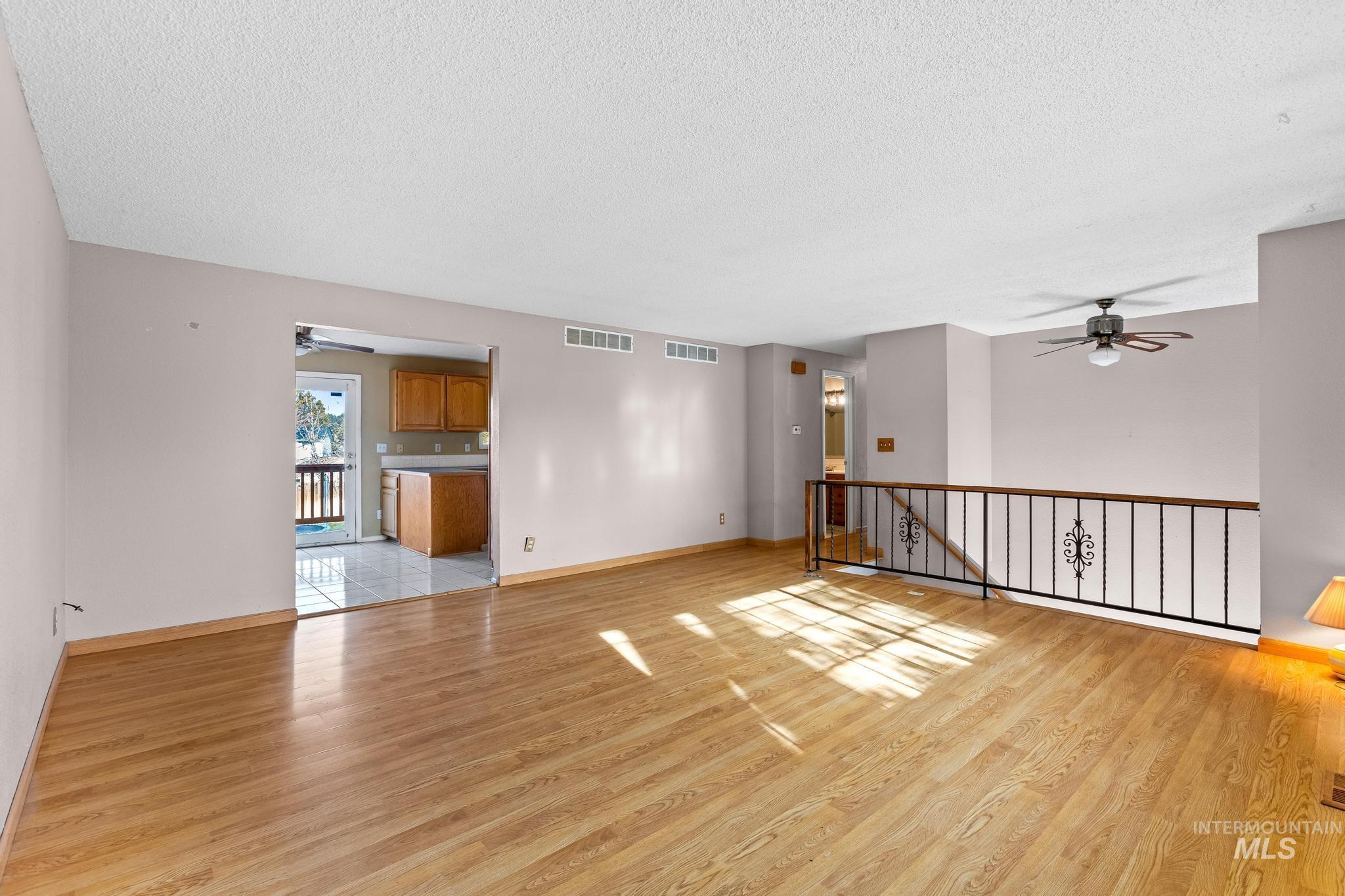 Empty room with a ceiling fan, a textured ceiling, and light wood-style floors