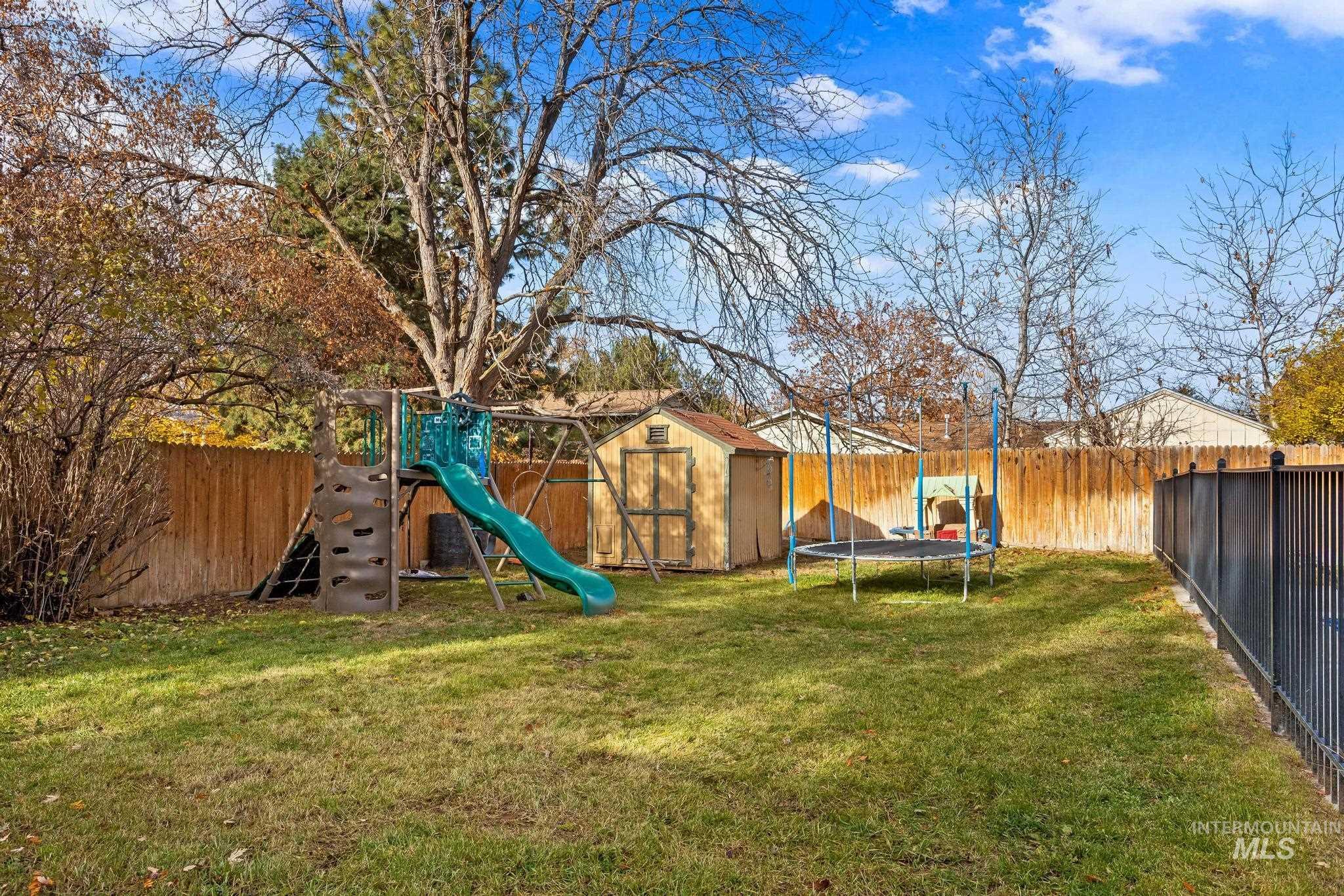 Fenced backyard with a trampoline, a playground, and a storage shed