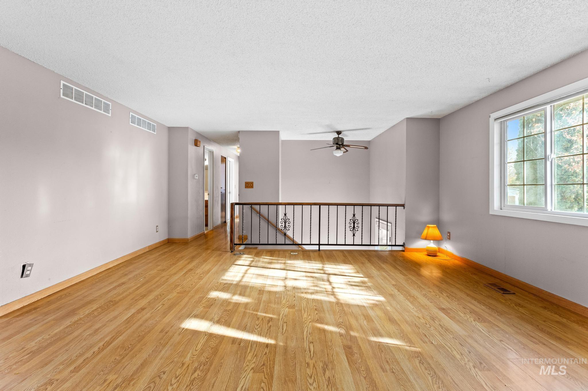 Empty room with light wood-type flooring, a textured ceiling, and ceiling fan