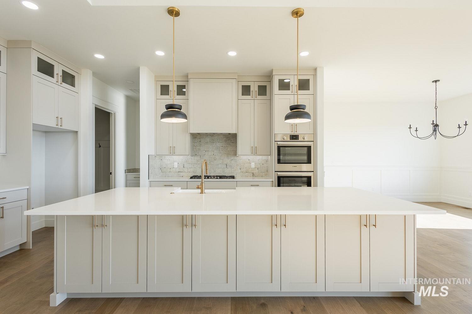 Kitchen featuring hanging light fixtures, decorative backsplash, light stone countertops, a large island, and glass insert cabinets