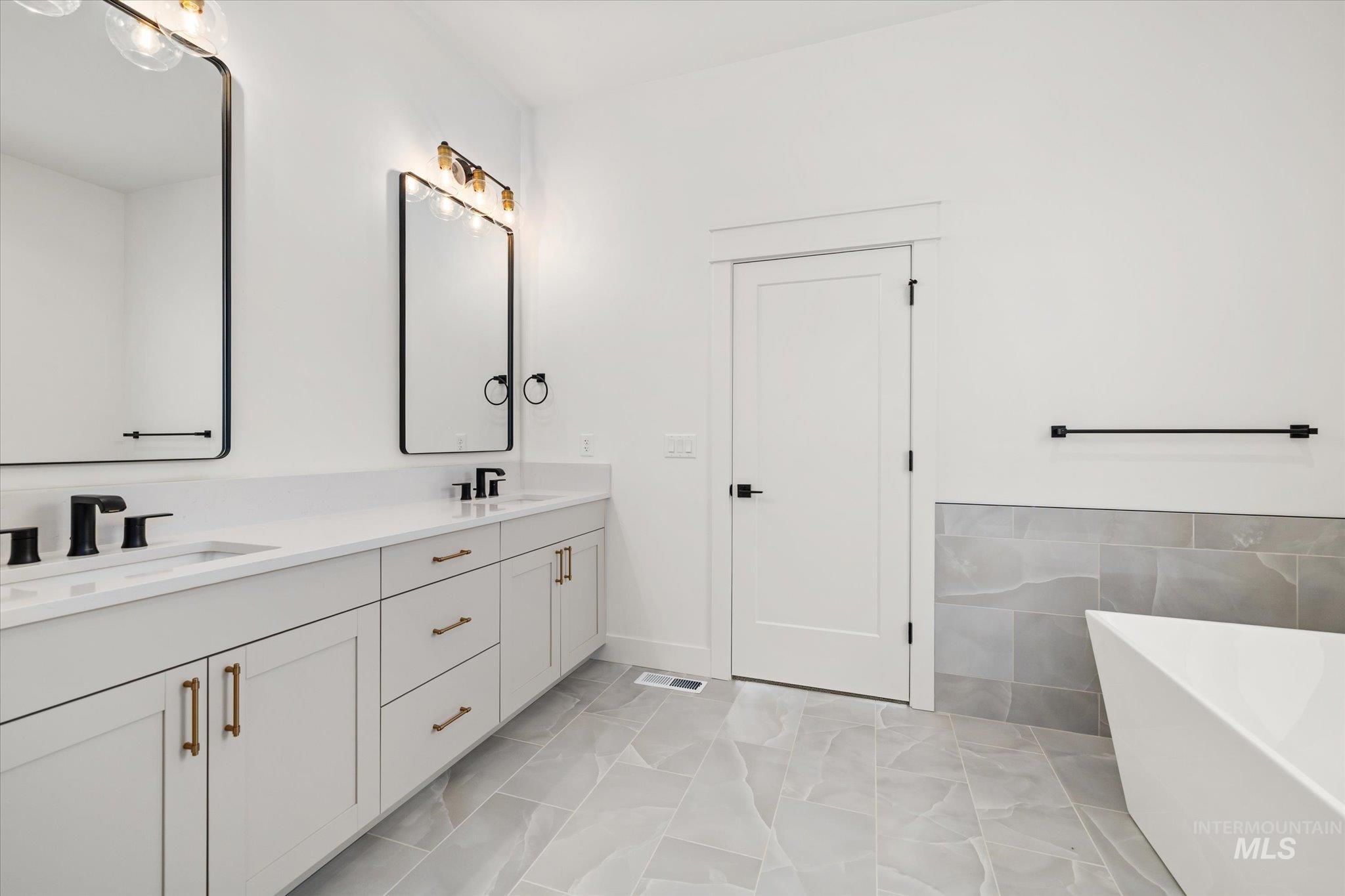 Full bathroom featuring a freestanding bath, double vanity, and tile walls