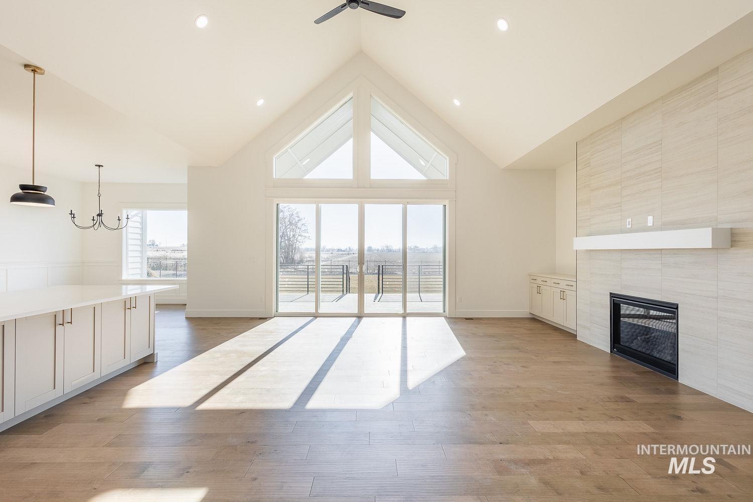 Unfurnished living room with high vaulted ceiling, healthy amount of natural light, light wood-style flooring, a tiled fireplace, and a chandelier