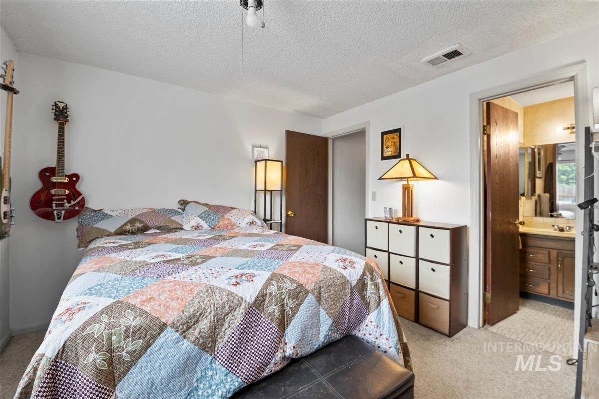 Bedroom featuring light colored carpet, a textured ceiling, and connected bathroom